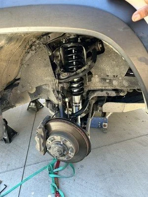 Close-up of a car's front suspension and brake system, showing the wheel removed to reveal the coil spring, shock absorber, brake rotor, and caliper.