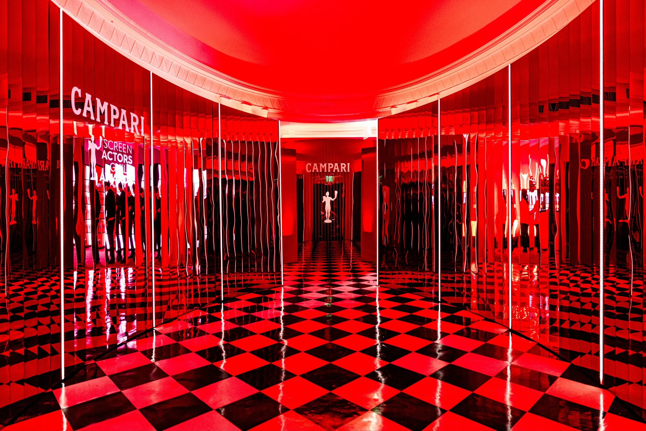 Interior of a vibrant red bar or lounge with reflective walls, checkered floor, and illuminated signs for Campari and Screen Actors Guild.