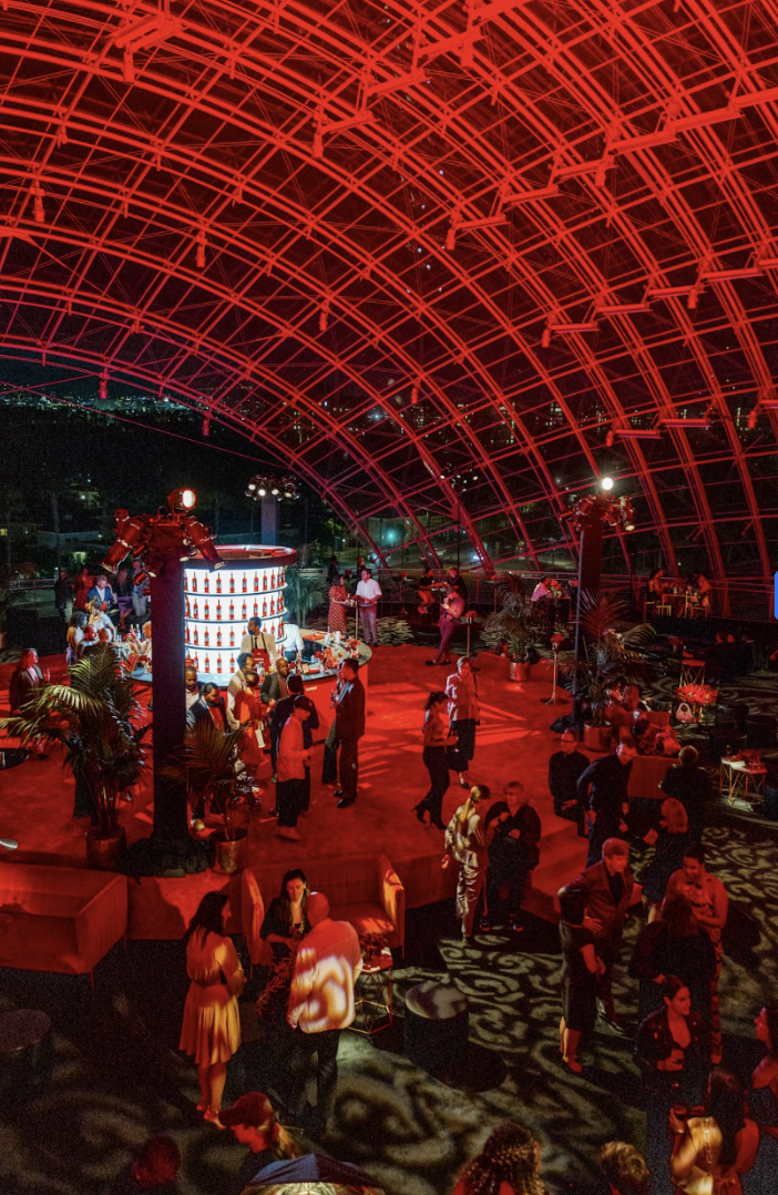 People dancing and socializing at a nightclub with a red-lit arched ceiling and a bar in the background.