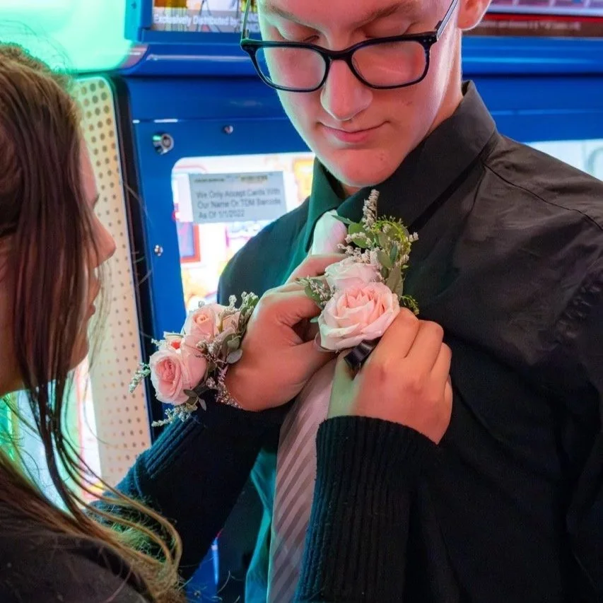 A person pinning a pink boutonniere with roses and greenery onto a man's suit jacket.