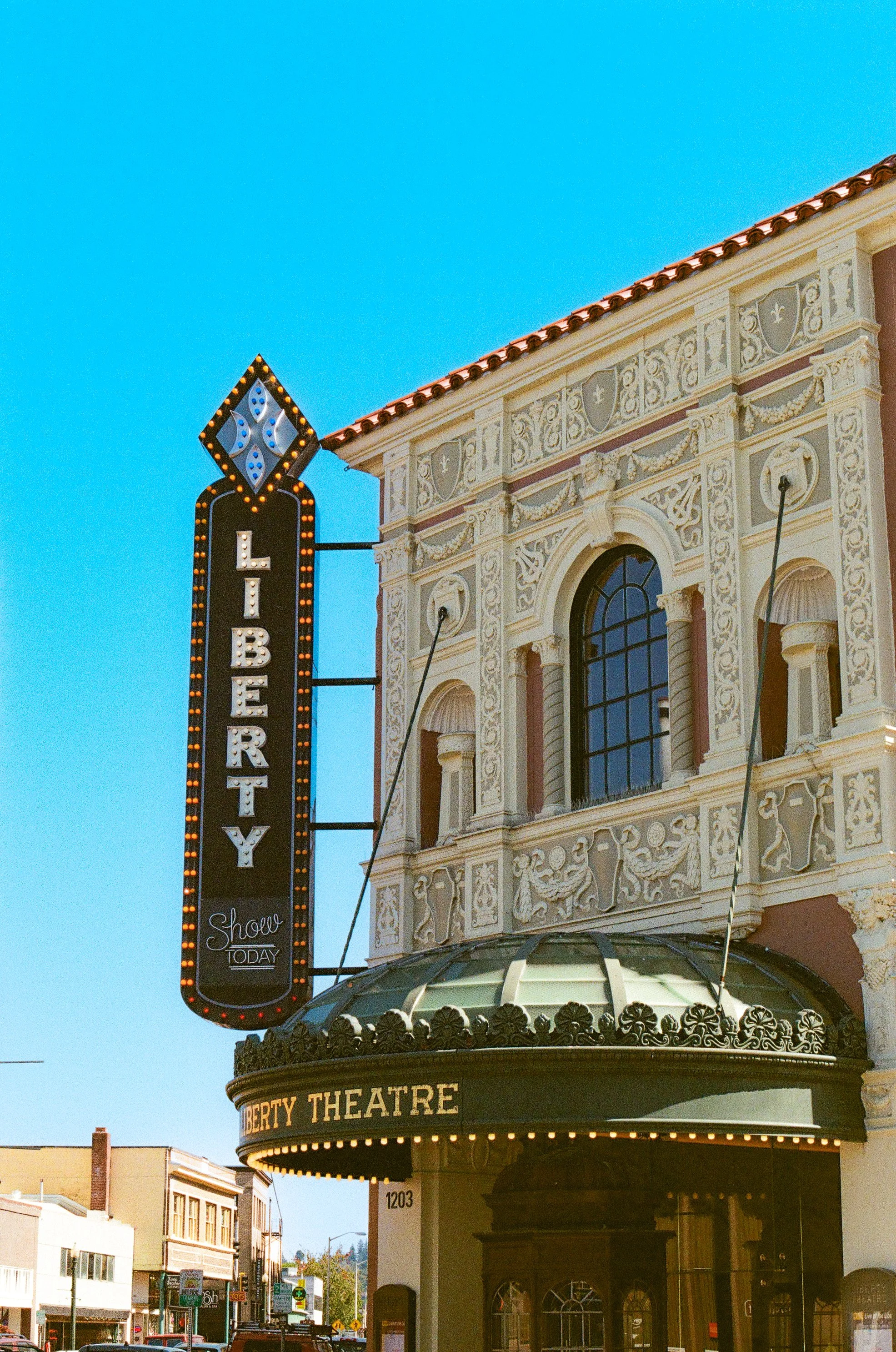 Facade of Liberty Theatre with ornate architecture, marquee, and vertical sign with the word 'LIBERTY' against a clear blue sky.