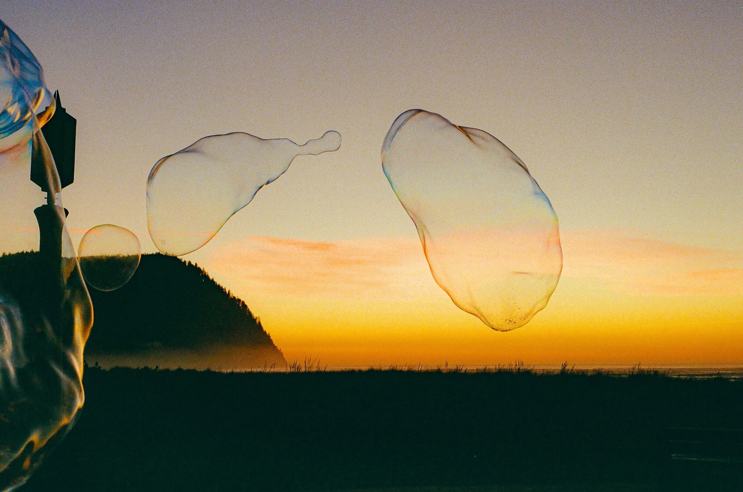 Soap bubbles floating in the air during sunset with a silhouette of a hill in the background.