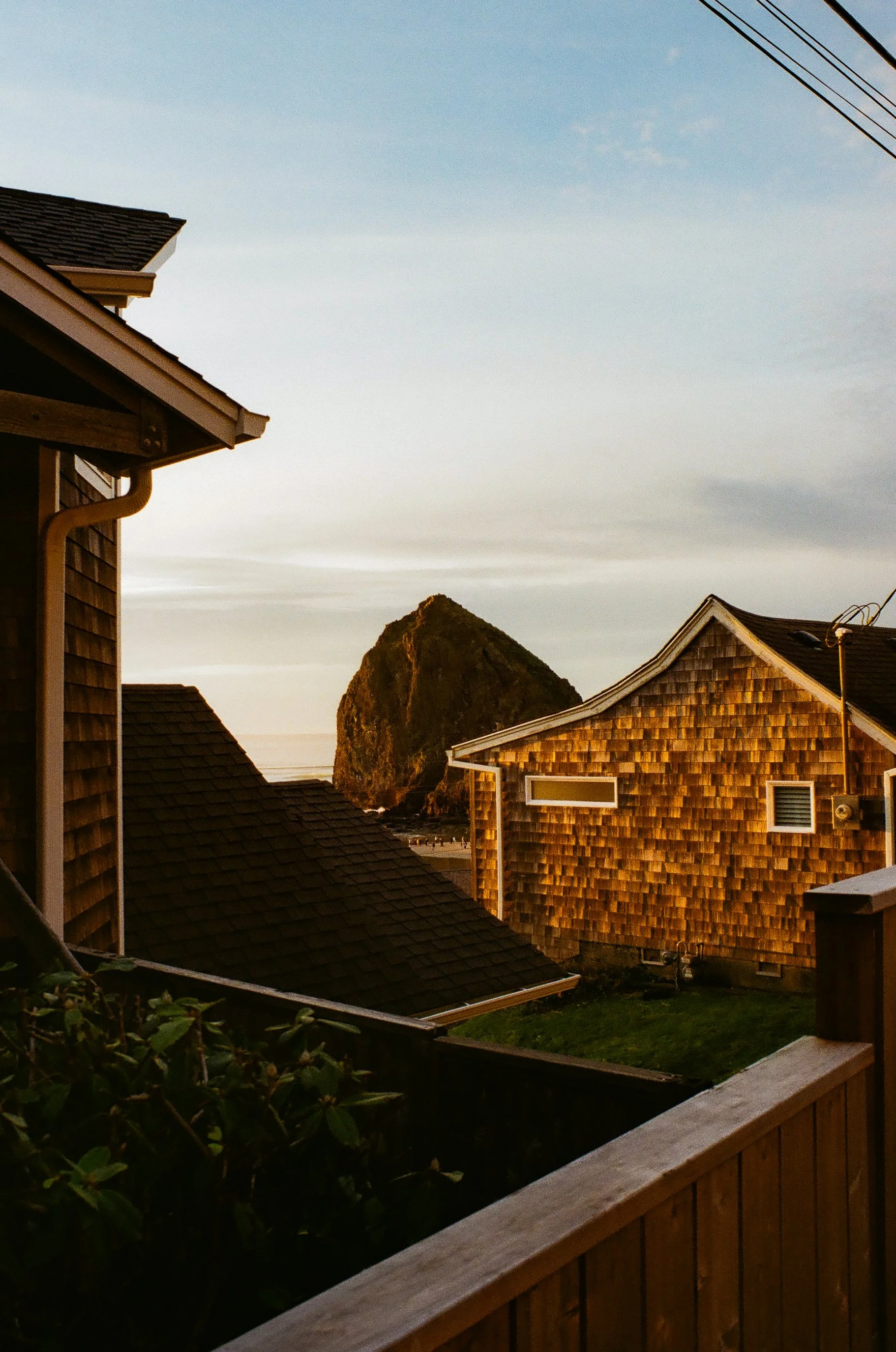 View of houses with shingle siding and a large rock formation in the distance, under a partly cloudy sky.