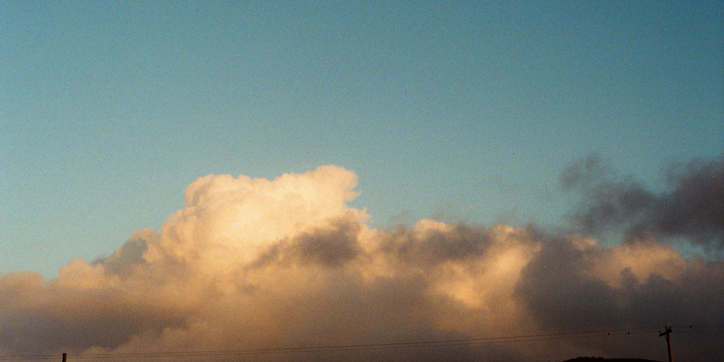 Sky with large, billowing clouds during sunset or sunrise, with a small portion of telephone poles or power lines at the bottom.