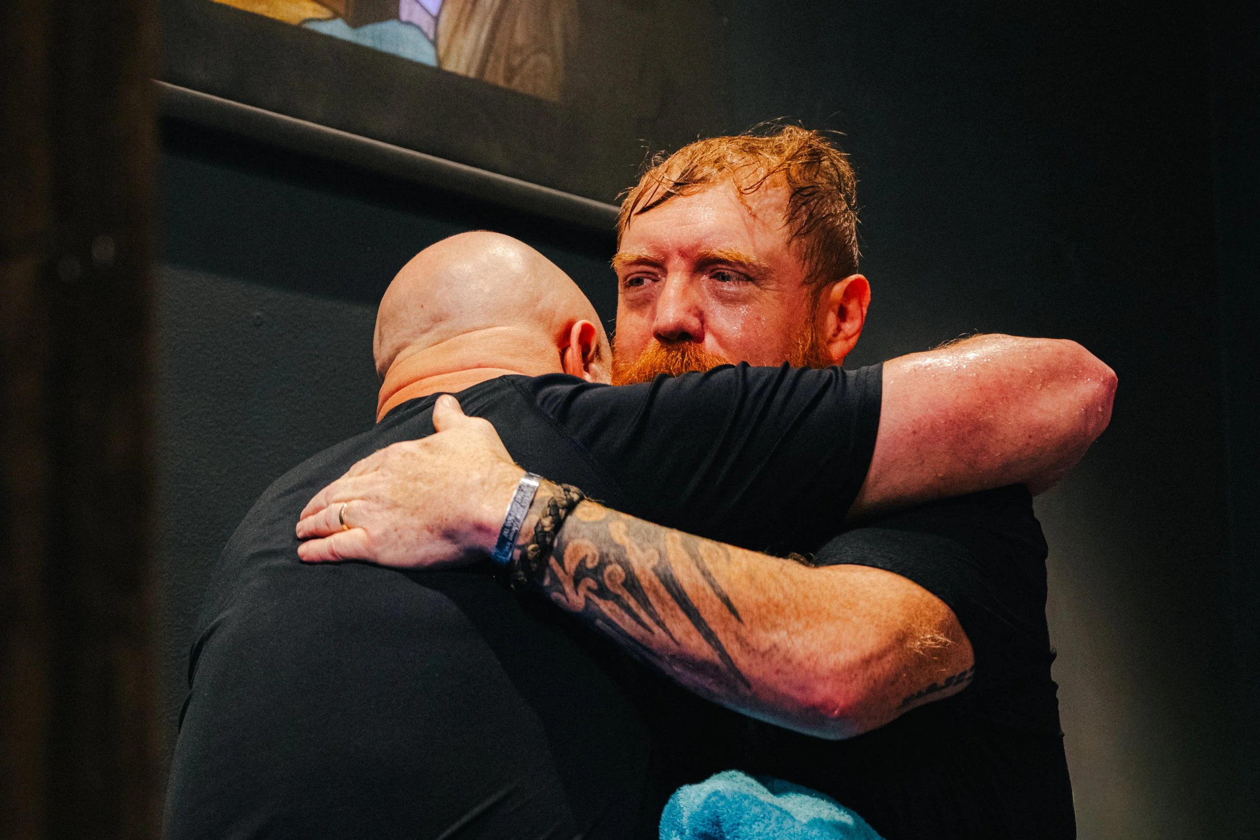 Two men hugging passionately, one with a bald head and the other with red hair and a beard, in an emotional moment.