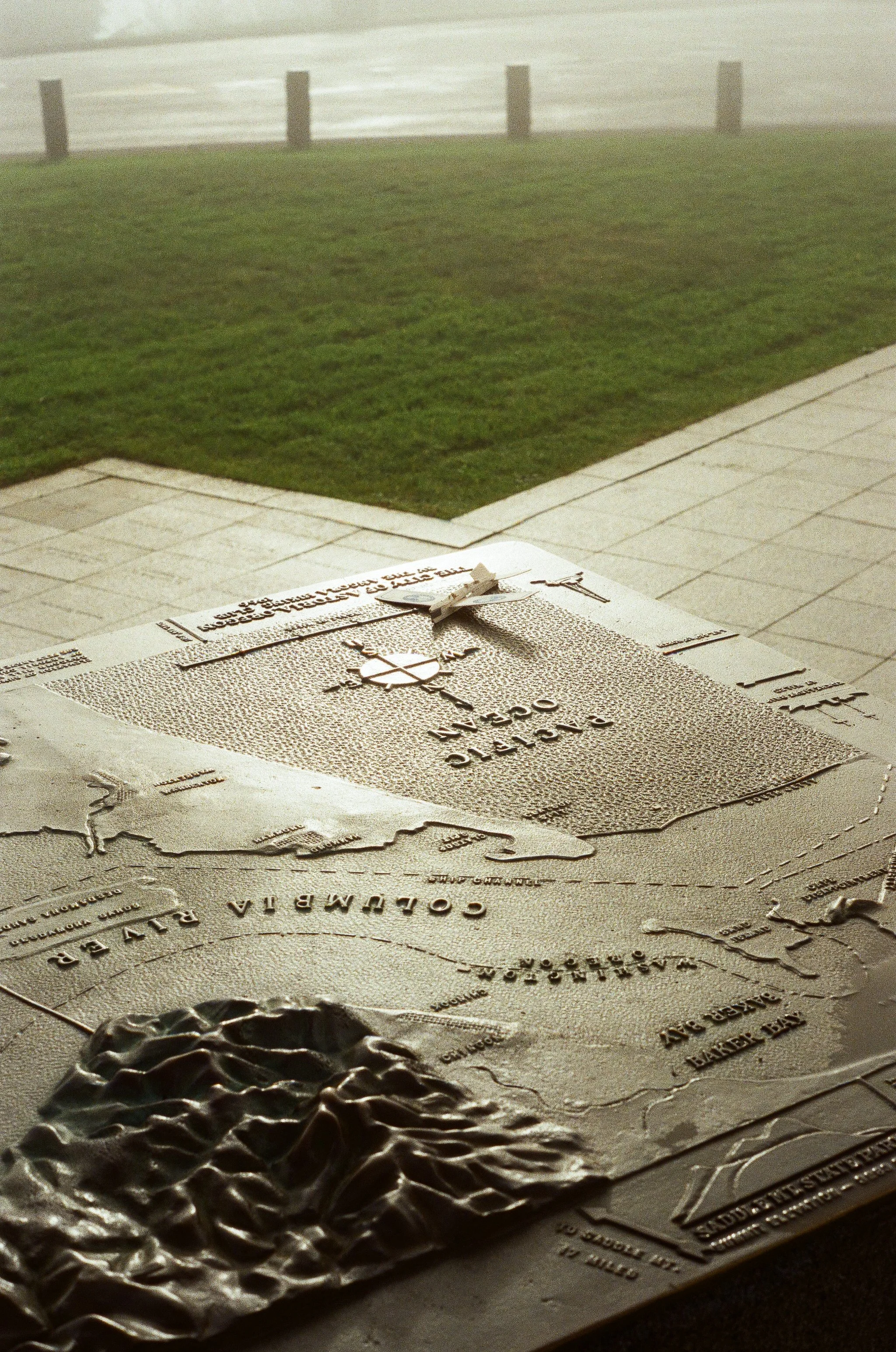 A detailed topographic map of Colombia and the surrounding regions lies on a table outside with a grassy area and a fence in the background.