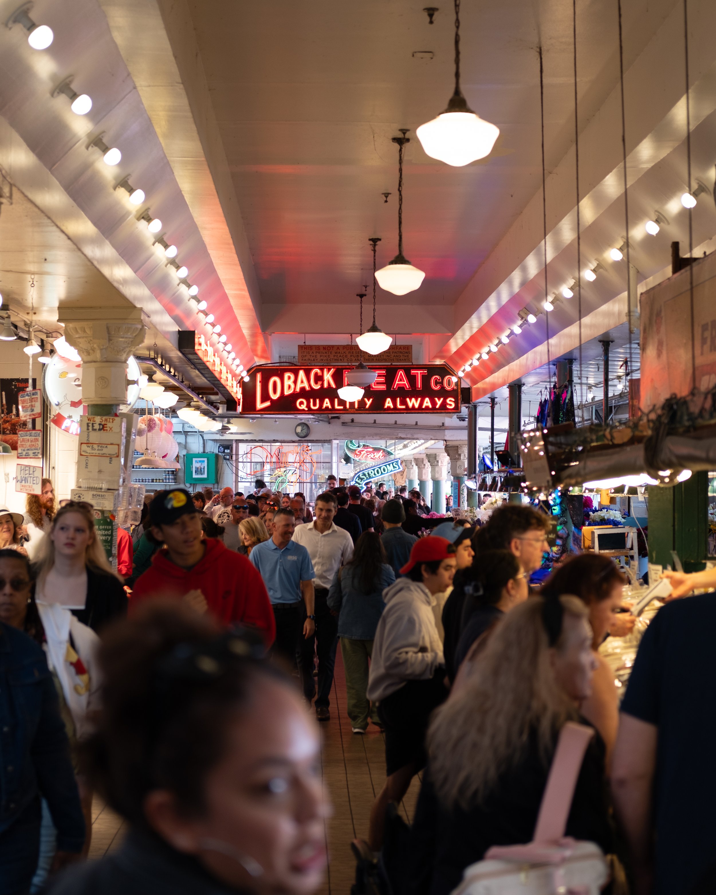 Crowded indoor marketplace with neon signs and bustling shoppers.