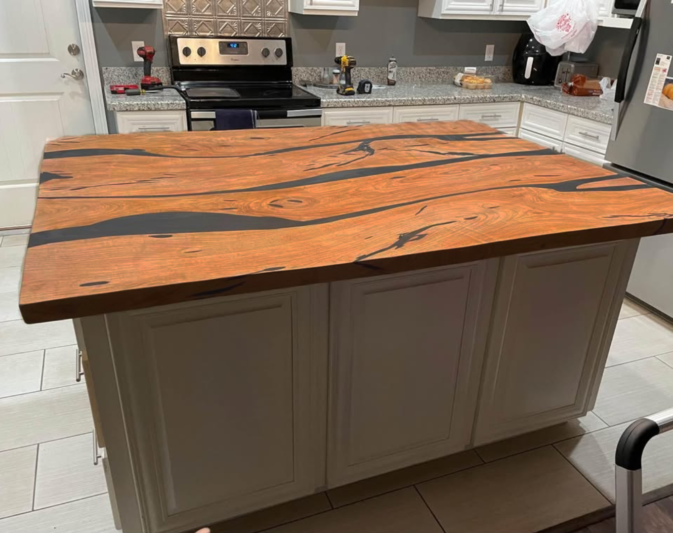 Kitchen island with a live edge wood countertop in a modern kitchen with white cabinets, gray countertops, and stainless steel appliances.