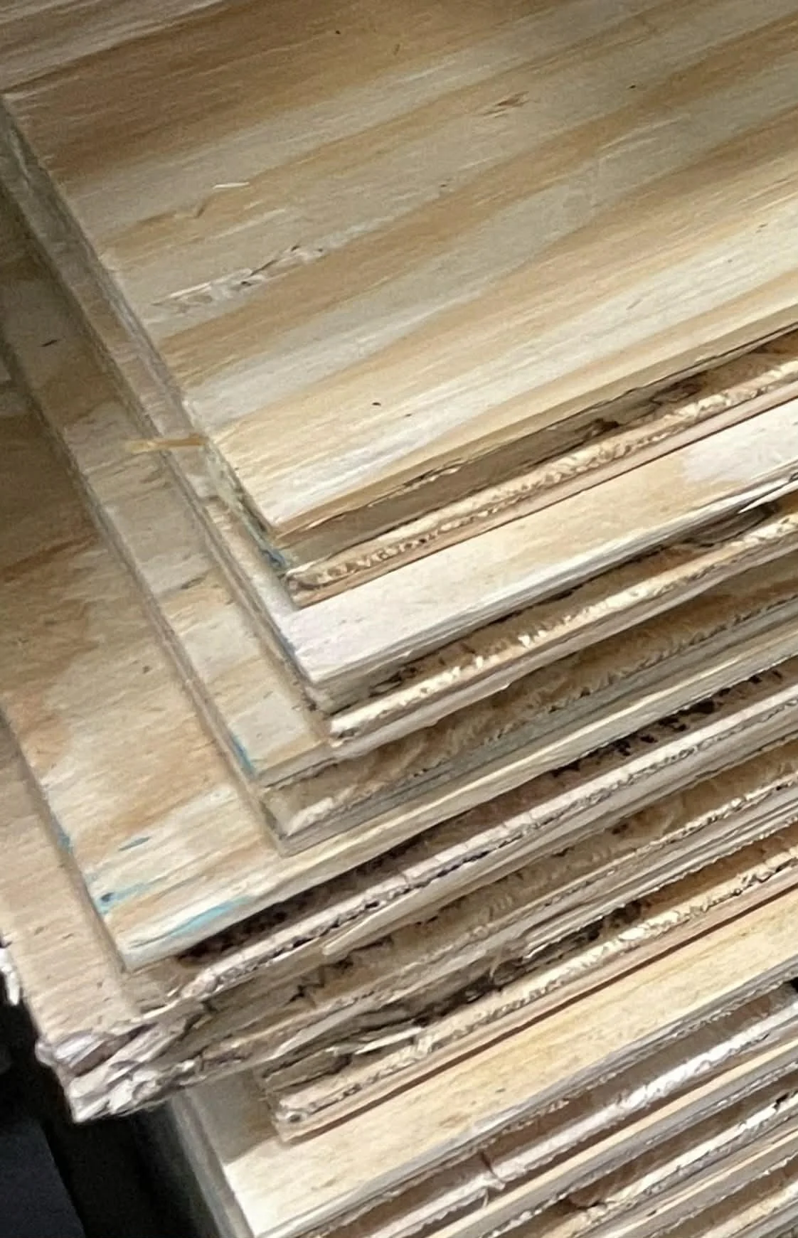 Stack of various light-colored plywood and particleboard sheets.