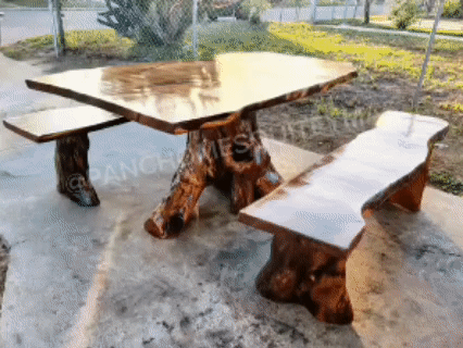 A wooden picnic table with a natural, irregular shape and a sturdy, artistic base, along with matching benches, set outdoors on a concrete surface.