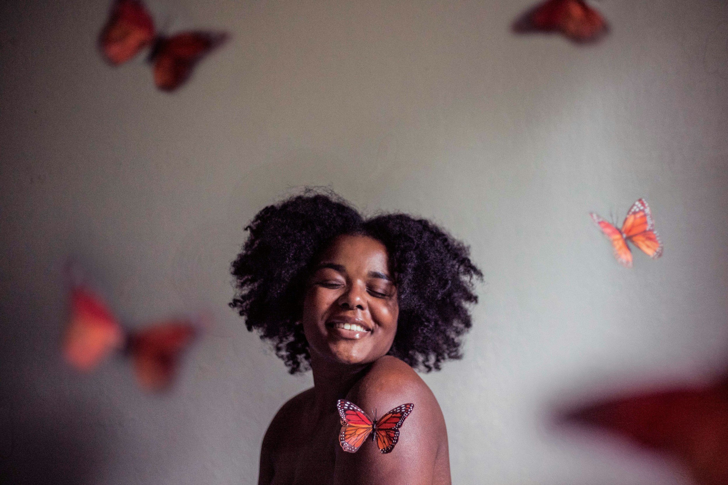 A woman with natural curly hair smiling with closed eyes, surrounded by orange and black butterflies.