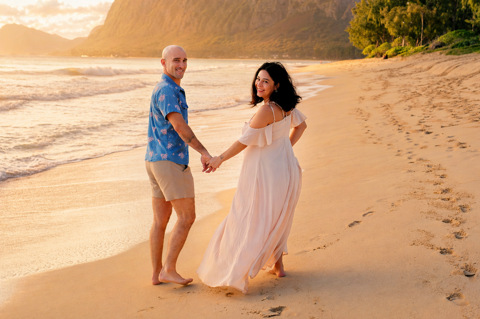 A happy couple holding hands and walking along a sandy beach during sunset, with green hills in the background.
