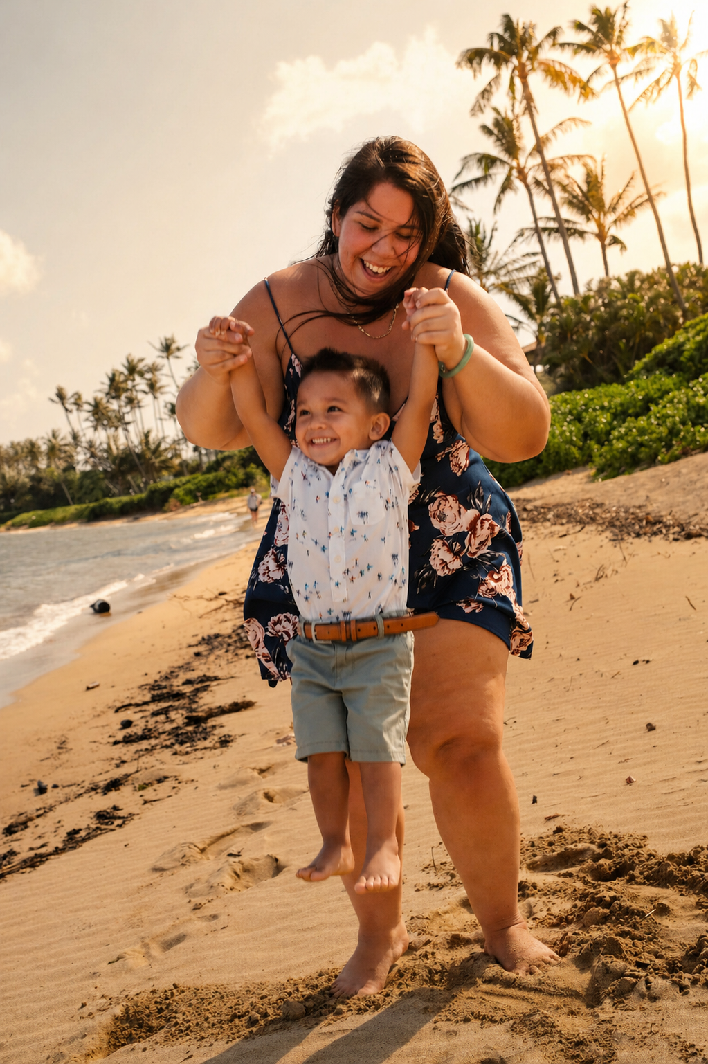A woman and a young boy are playing and smiling on a sandy beach with palm trees and an ocean in the background during sunset.