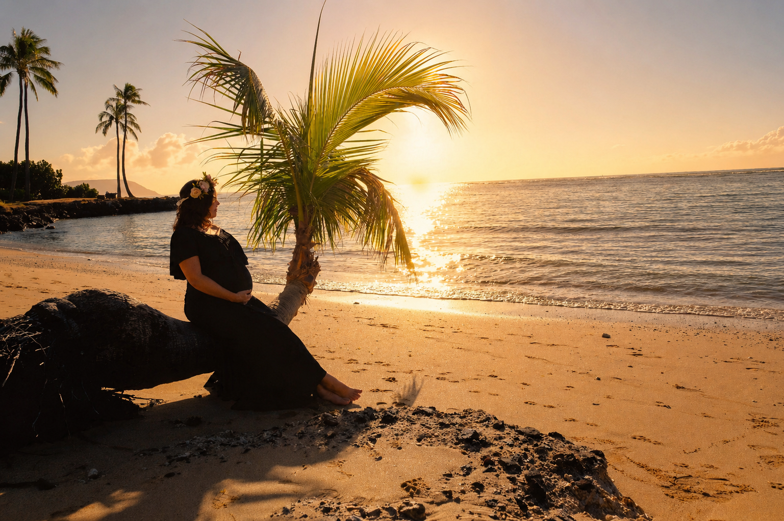 A pregnant woman sitting on a fallen palm tree on a sandy beach during sunset, with a palm tree beside her and the ocean in the background.