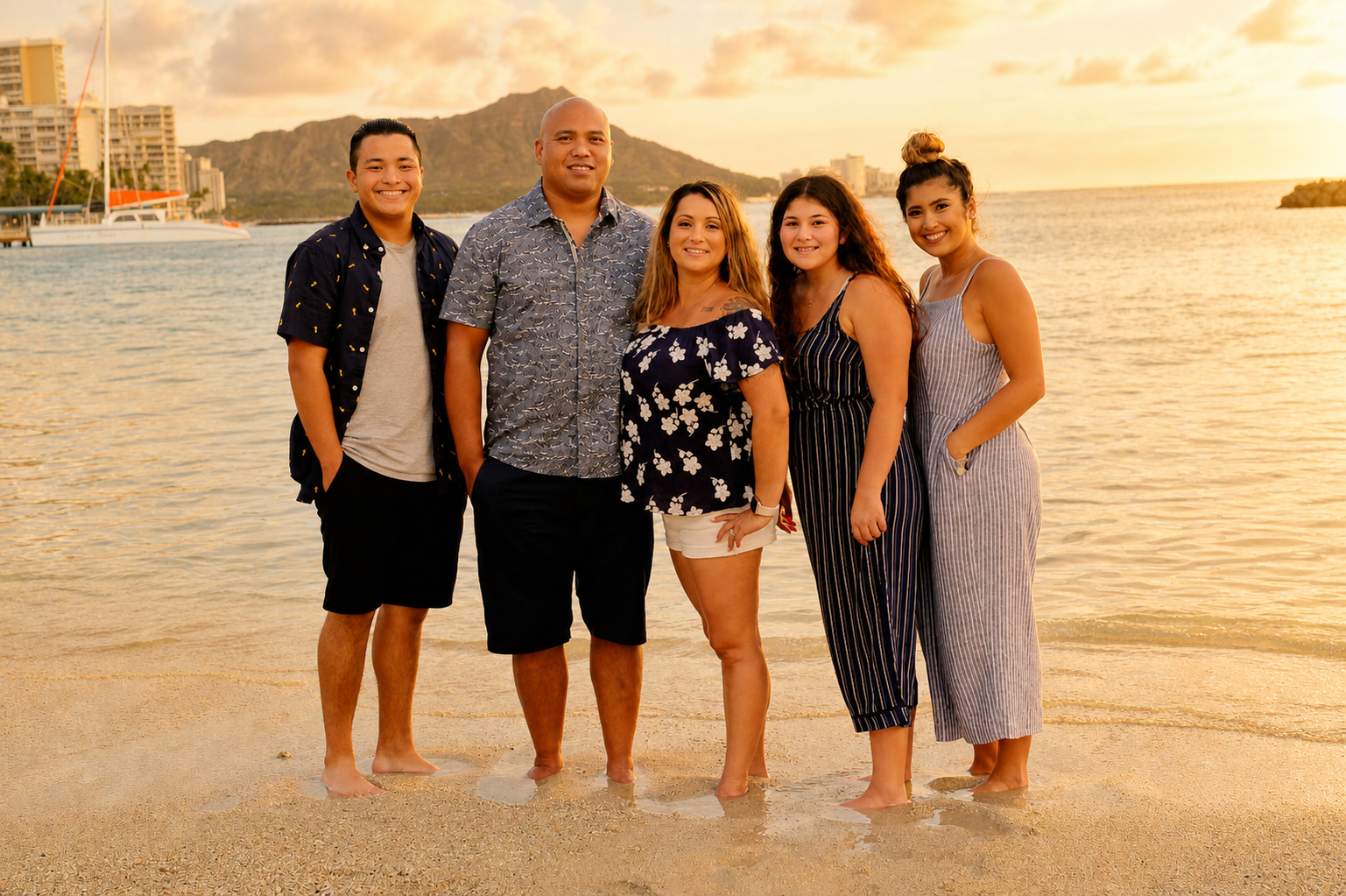 A group of six people standing on a beach at sunset, with water, sailboats, mountains, and buildings in the background.
