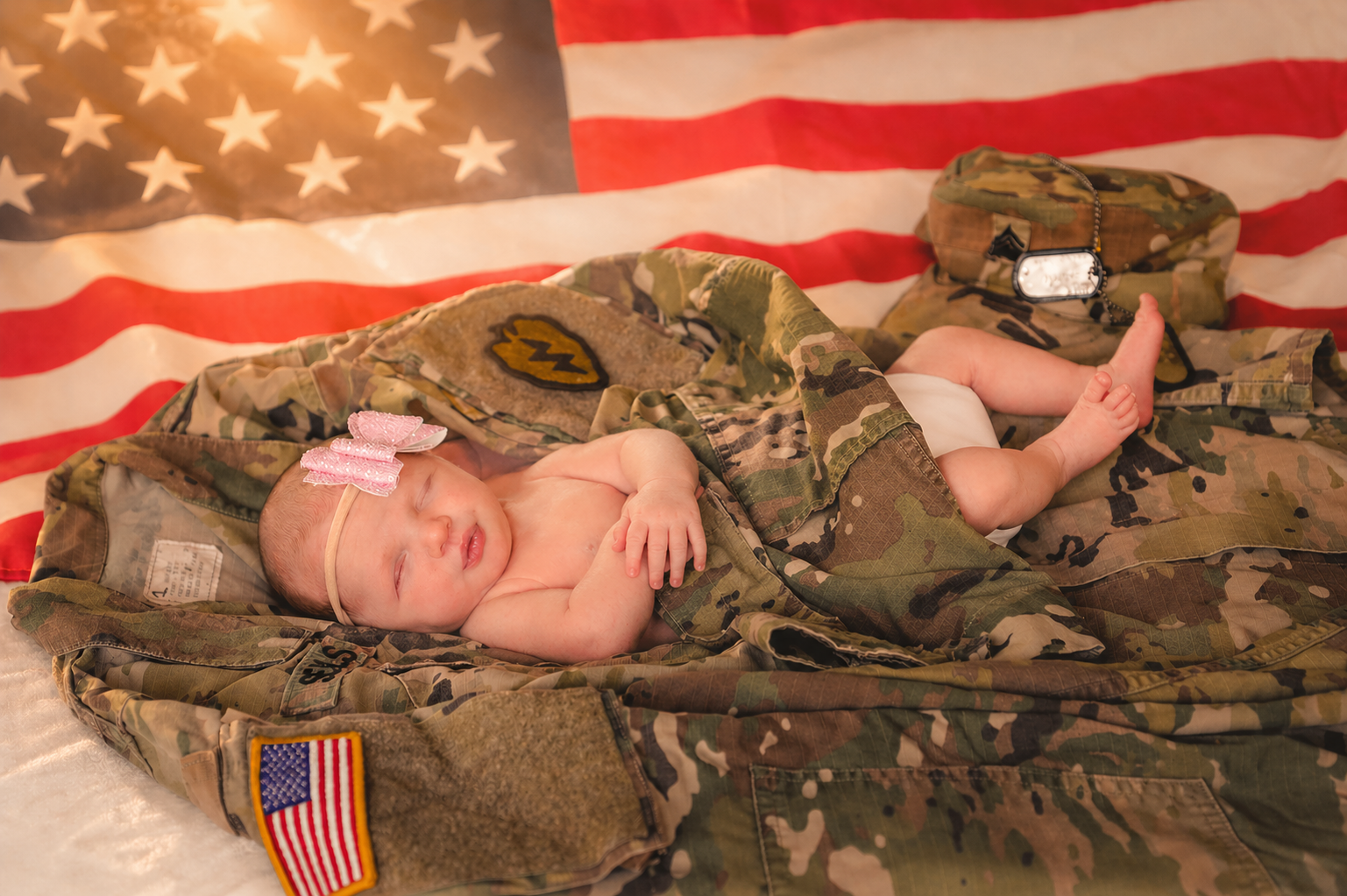 A sleeping baby lying on a blanket and surrounded by military gear, with an American flag in the background.
