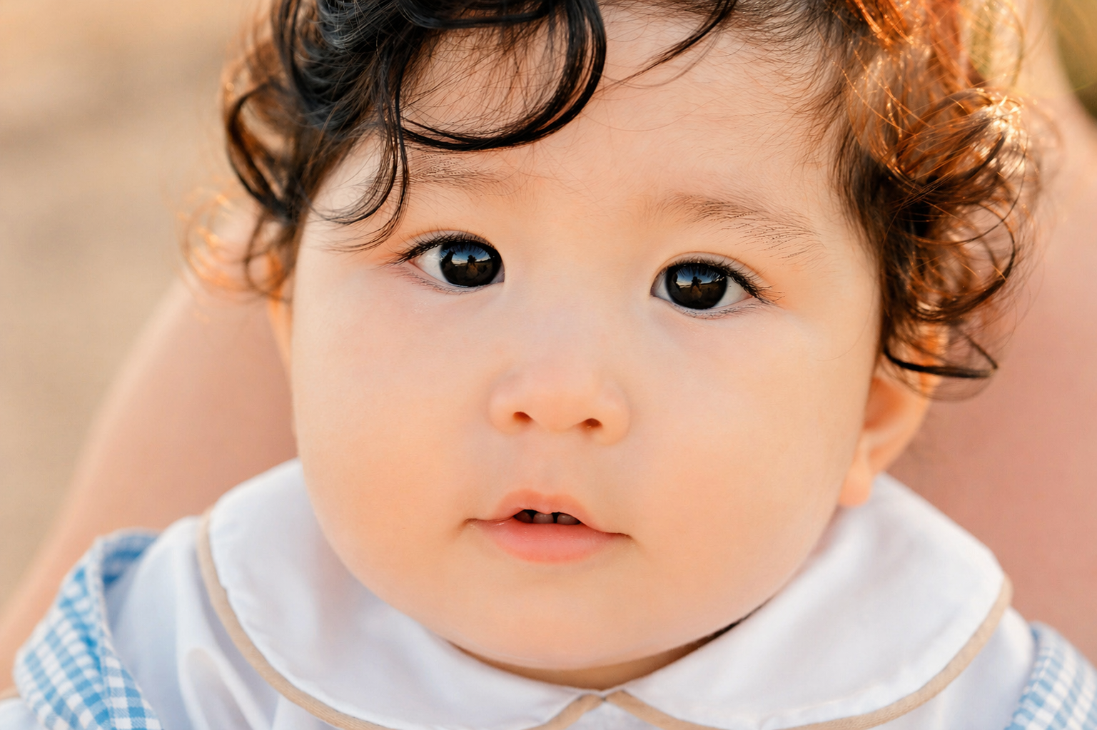 Close-up of a young child with curly brown hair and dark eyes, looking into the camera, with a blurred background.