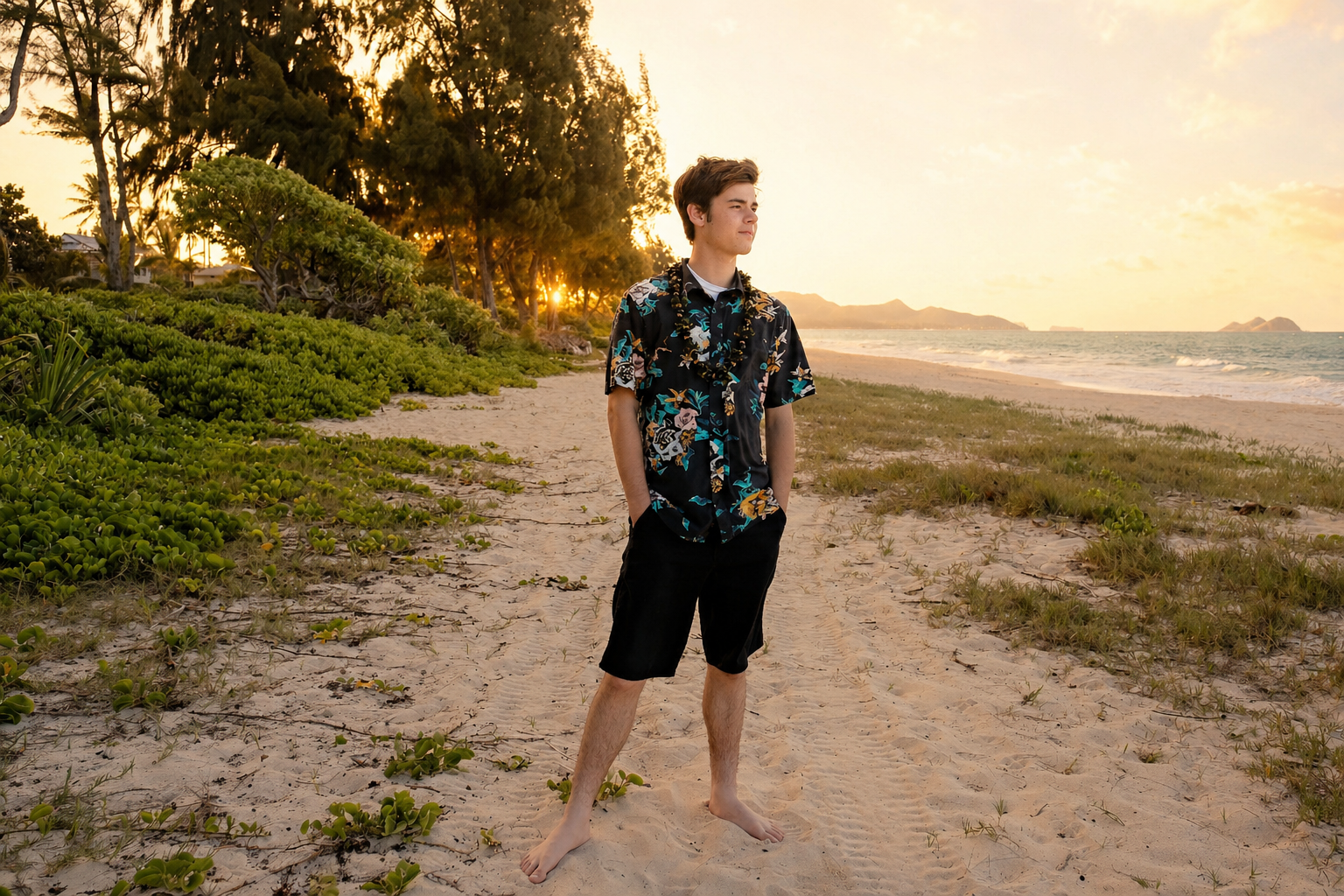 A young man standing on a sandy beach during sunset, wearing a floral shirt and black shorts, with his hands in his pockets, looking thoughtfully into the distance.