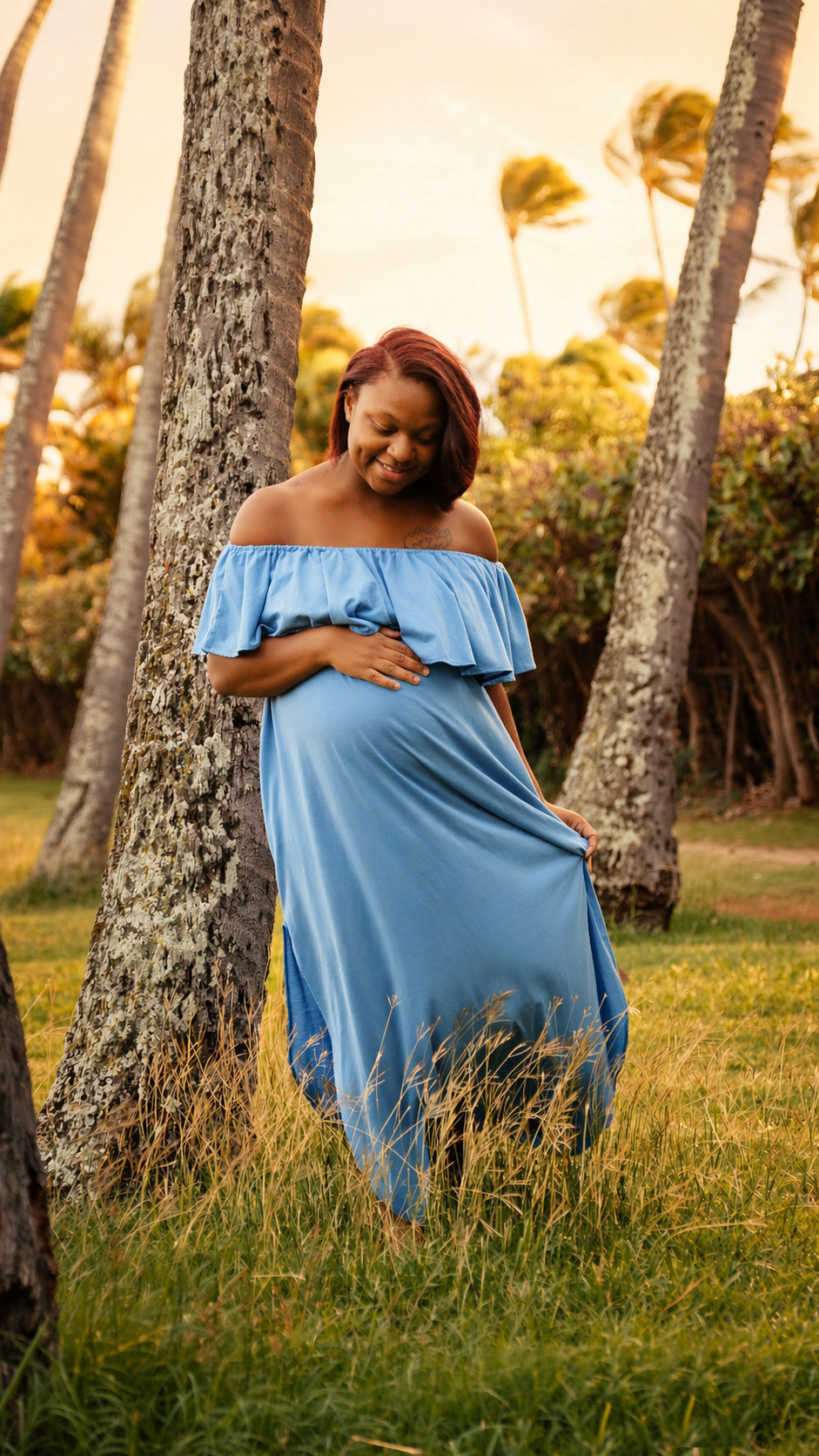 A pregnant woman in a blue dress standing outdoors among trees, smiling and holding her belly.