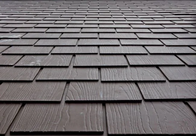 Close-up view of brown, wooden-textured shingle roofing on a building, with shingles arranged in horizontal rows.
