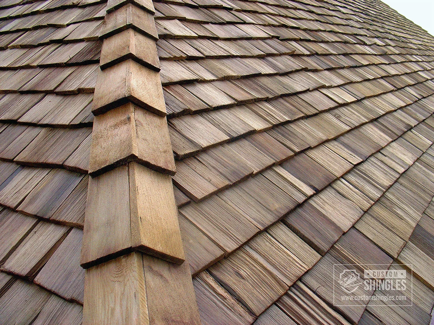 Close-up of a shingled roof with wooden shingles and a vertical wooden ridge.
