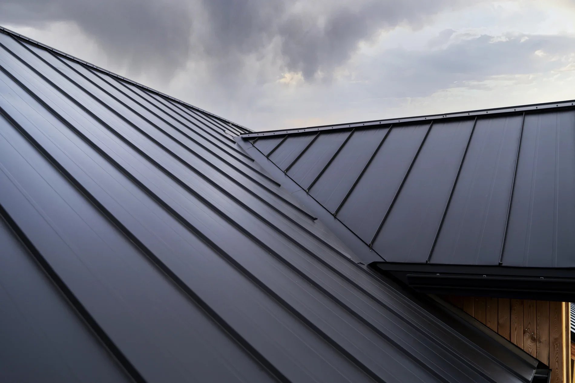 Close-up view of a modern metal roof with intersecting sloped sections and cloudy sky in the background.