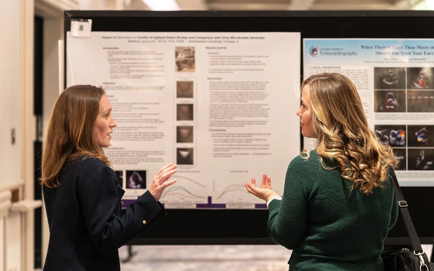 Two women engaged in conversation in front of a scientific poster at a conference or academic event.