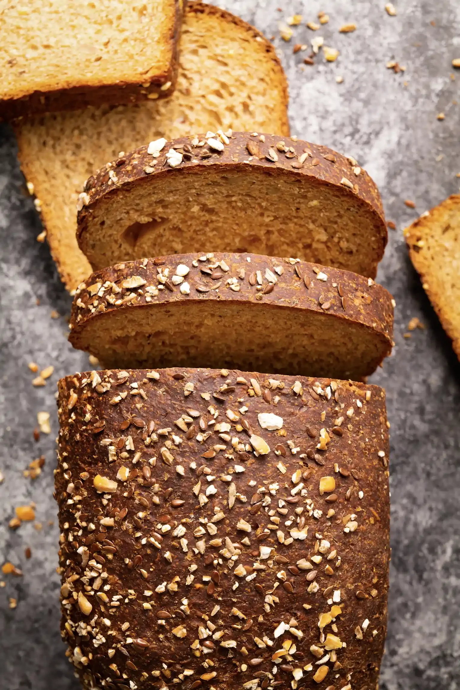 Sliced loaf of multigrain bread with a seeded crust on a gray surface. By New Jersey food photographer & food stylist team Bartholomew Studio.