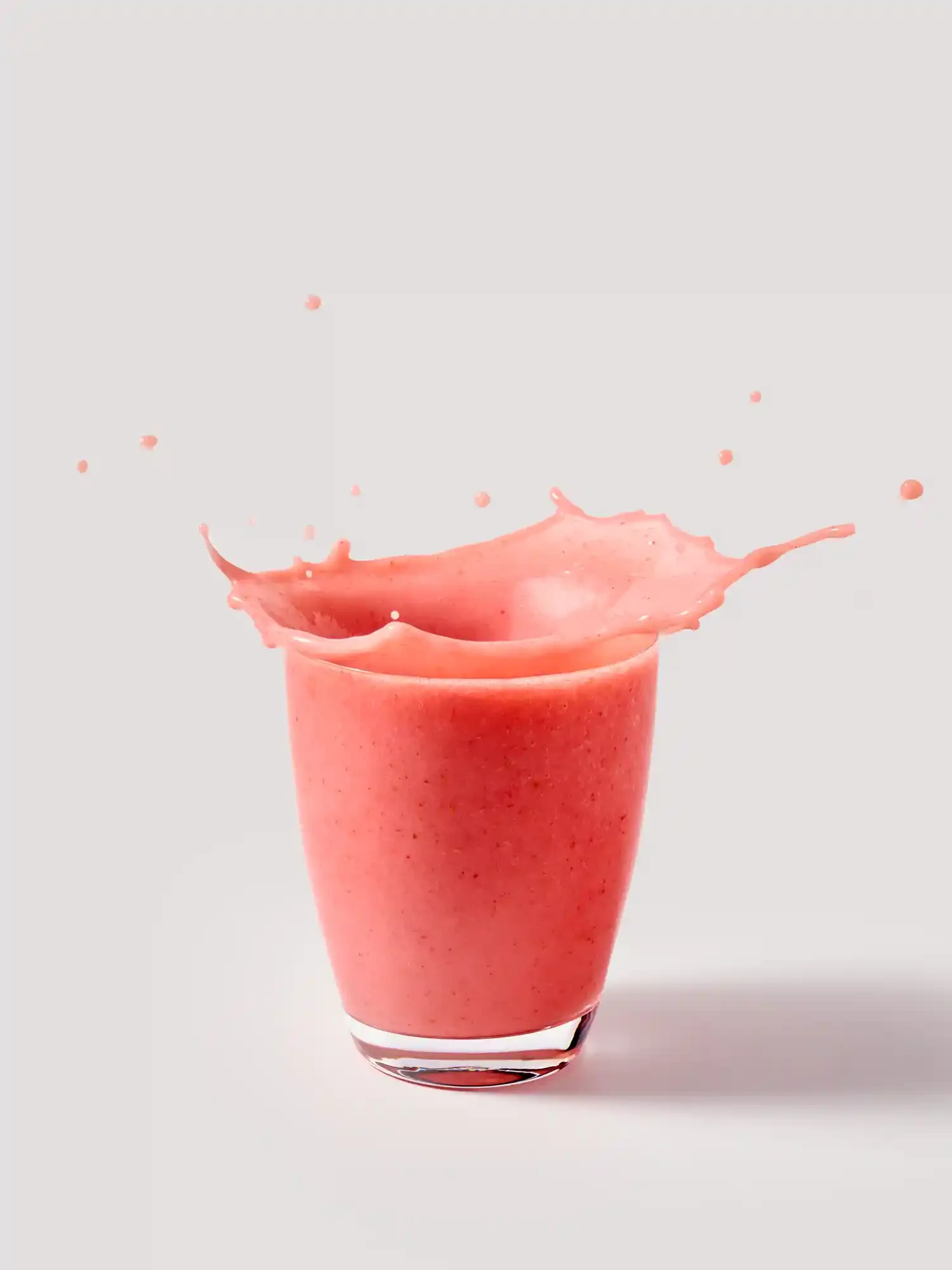 A pink smoothie in a clear glass with splash and droplets flying out. By drink splash photographer & stylist team Bartholomew Studio.
