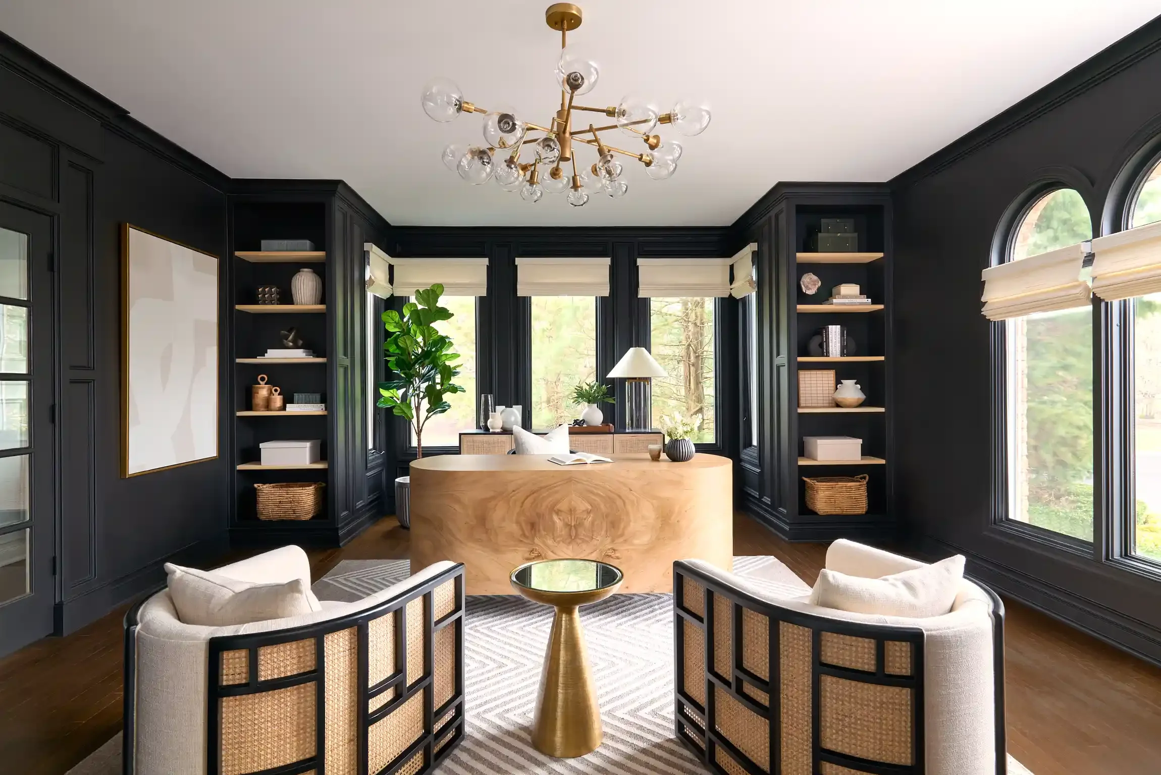 Living room with black paneling, large windows, modern chandelier, light wood desk, two white armchairs, and various decorative items. By NY & NJ interior photographer Bartholomew Studio.