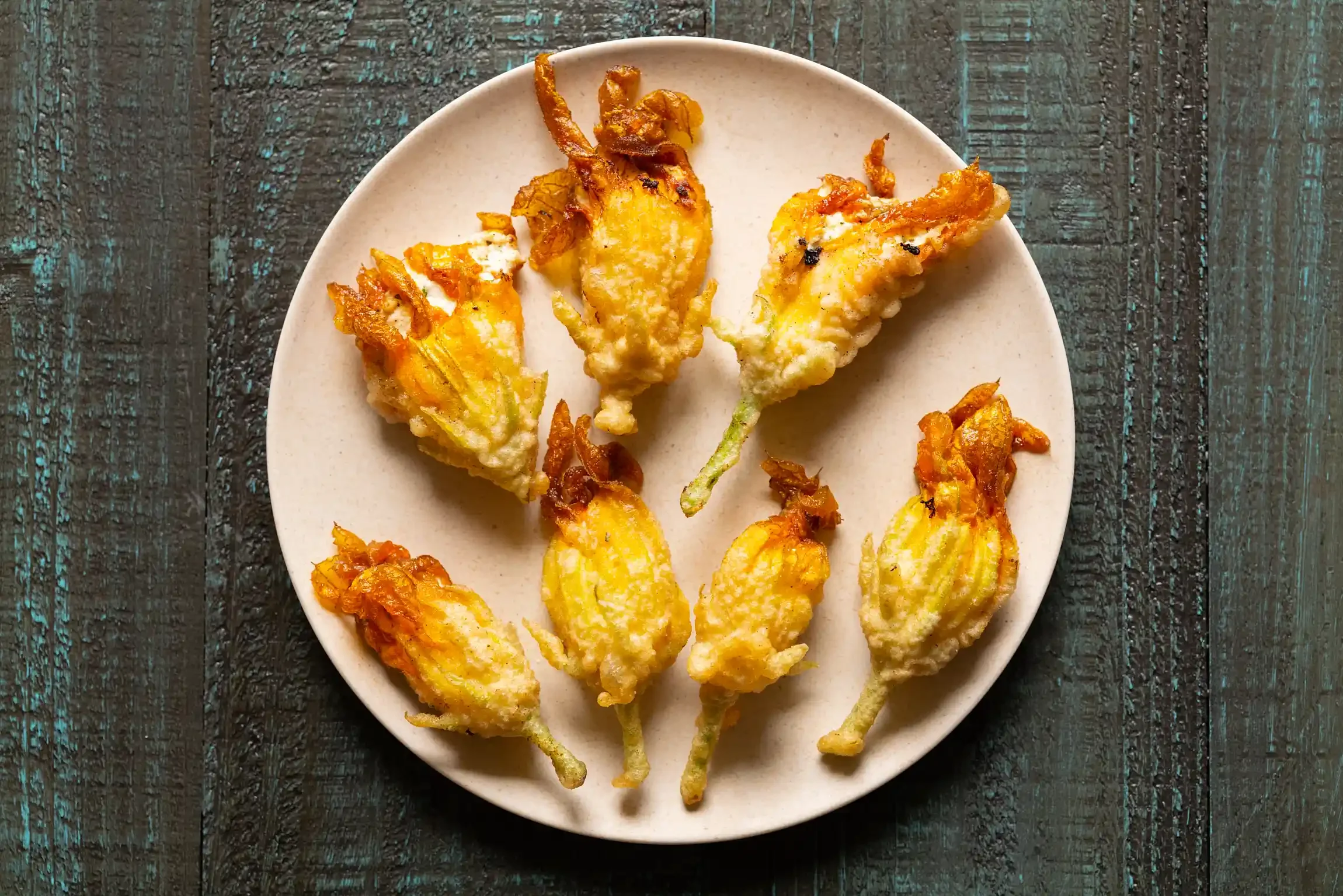 Deep-fried squash blossoms on a beige plate, placed on a dark wooden surface. By NYC, PA & NJ food photographer & food stylist team Bartholomew Studio.
