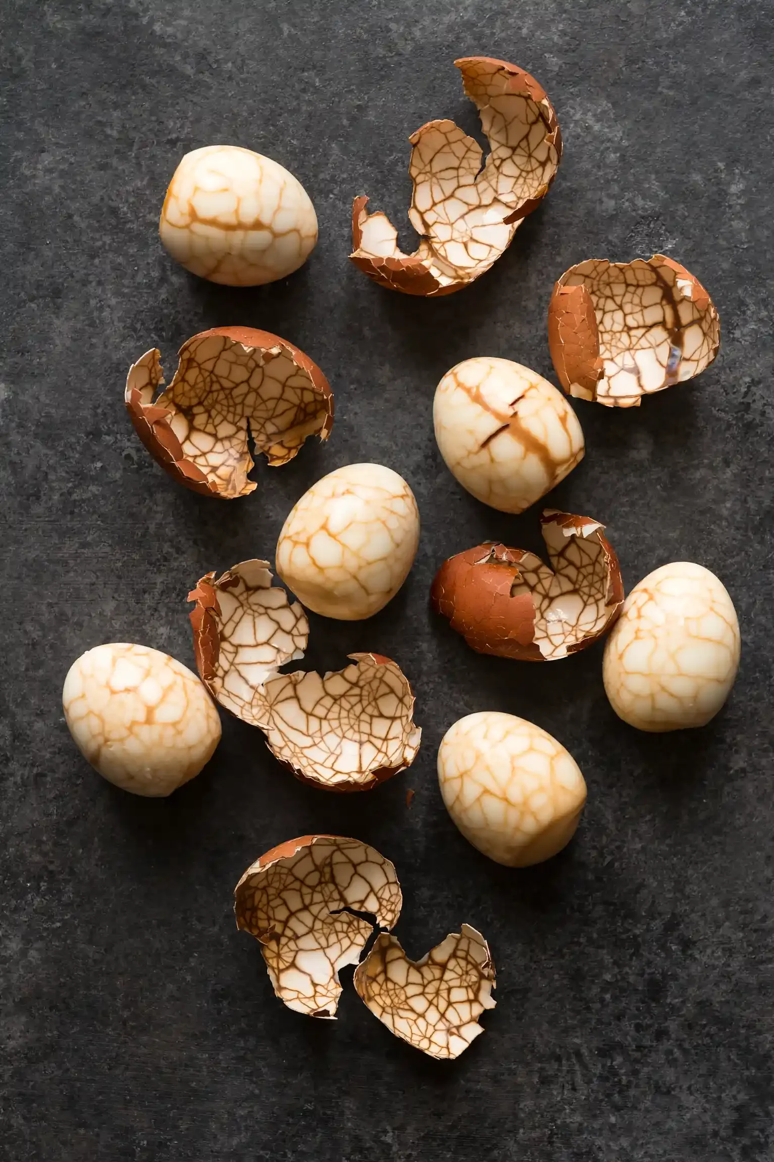 Tea Marbled Eggs scattered on a dark surface, some broken into pieces. By Philadelphia, PA food photographer & food stylist team Bartholomew Studio.