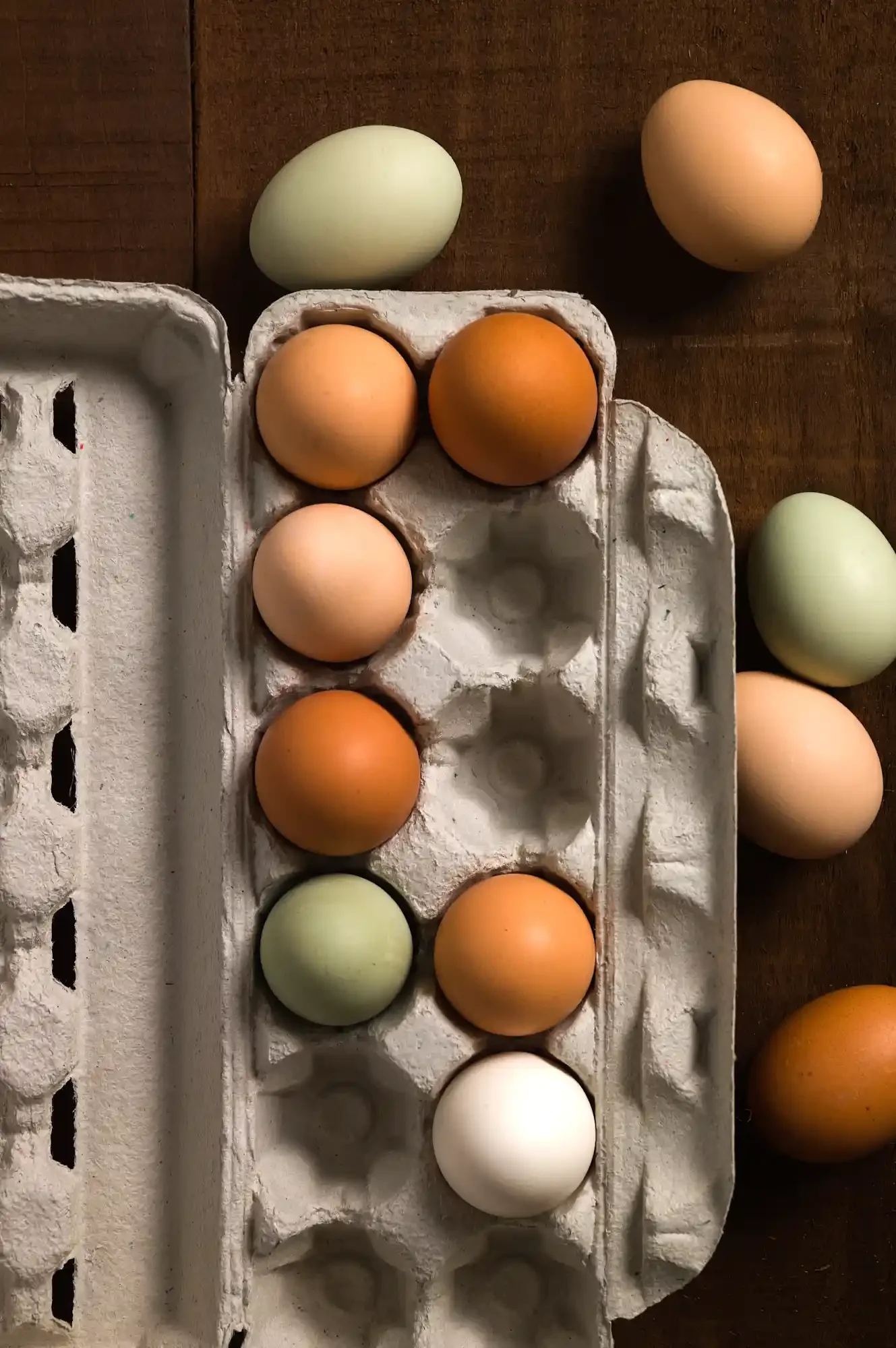 A carton of eggs with some eggs outside of it on a wooden surface. By Bucks County, PA food photographer & food stylist team Bartholomew Studio.