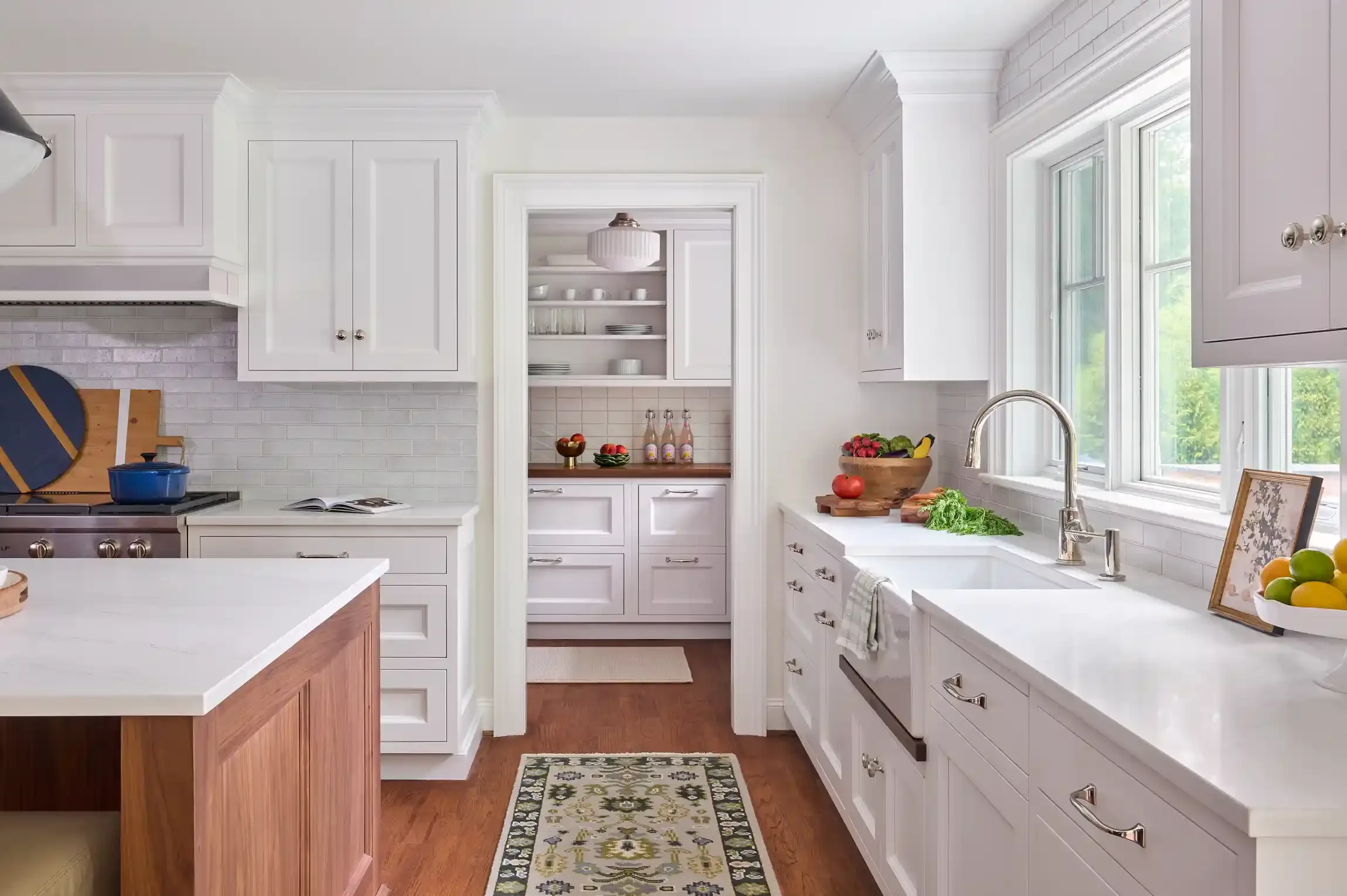 Bright kitchen with white cabinets, a window over the sink, and a wooden island in the foreground. By New Jersey interior design photographer Bartholomew Studio.