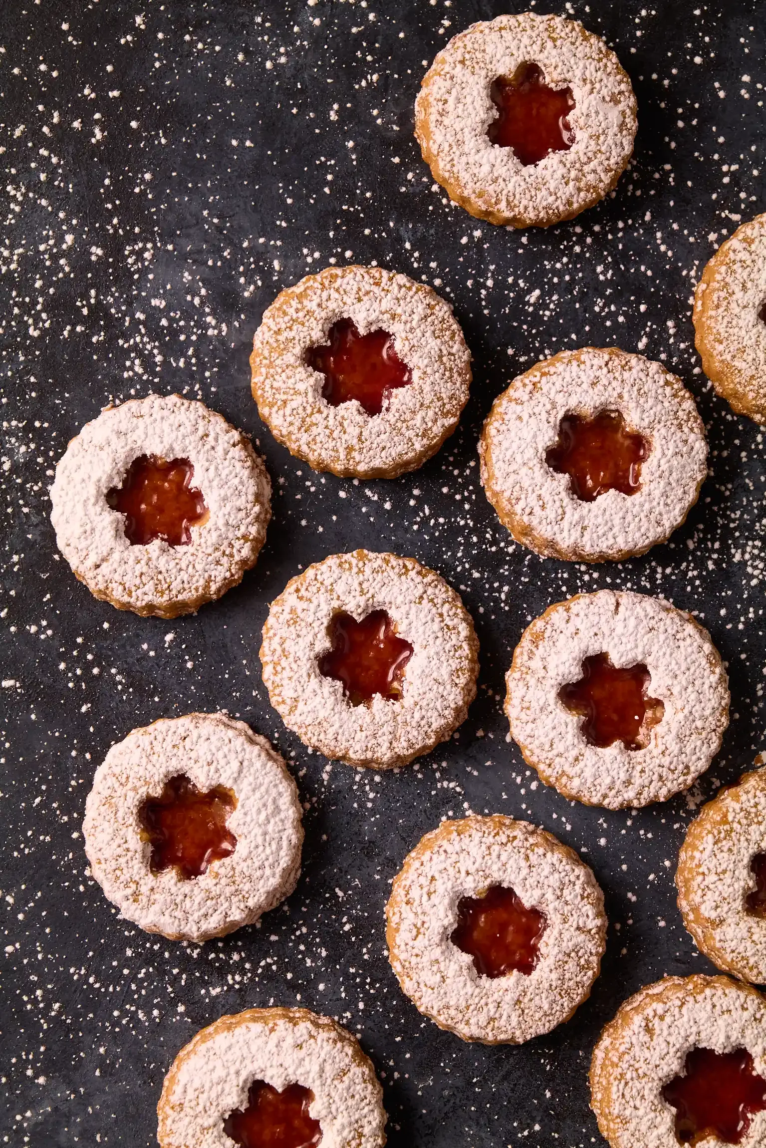 Austrian Linzer Cookies with powdered sugar and a star-shaped jam filling, arranged on a dark surface. By Philadelphia, PA & NJ food photographer & food stylist team Bartholomew Studio.