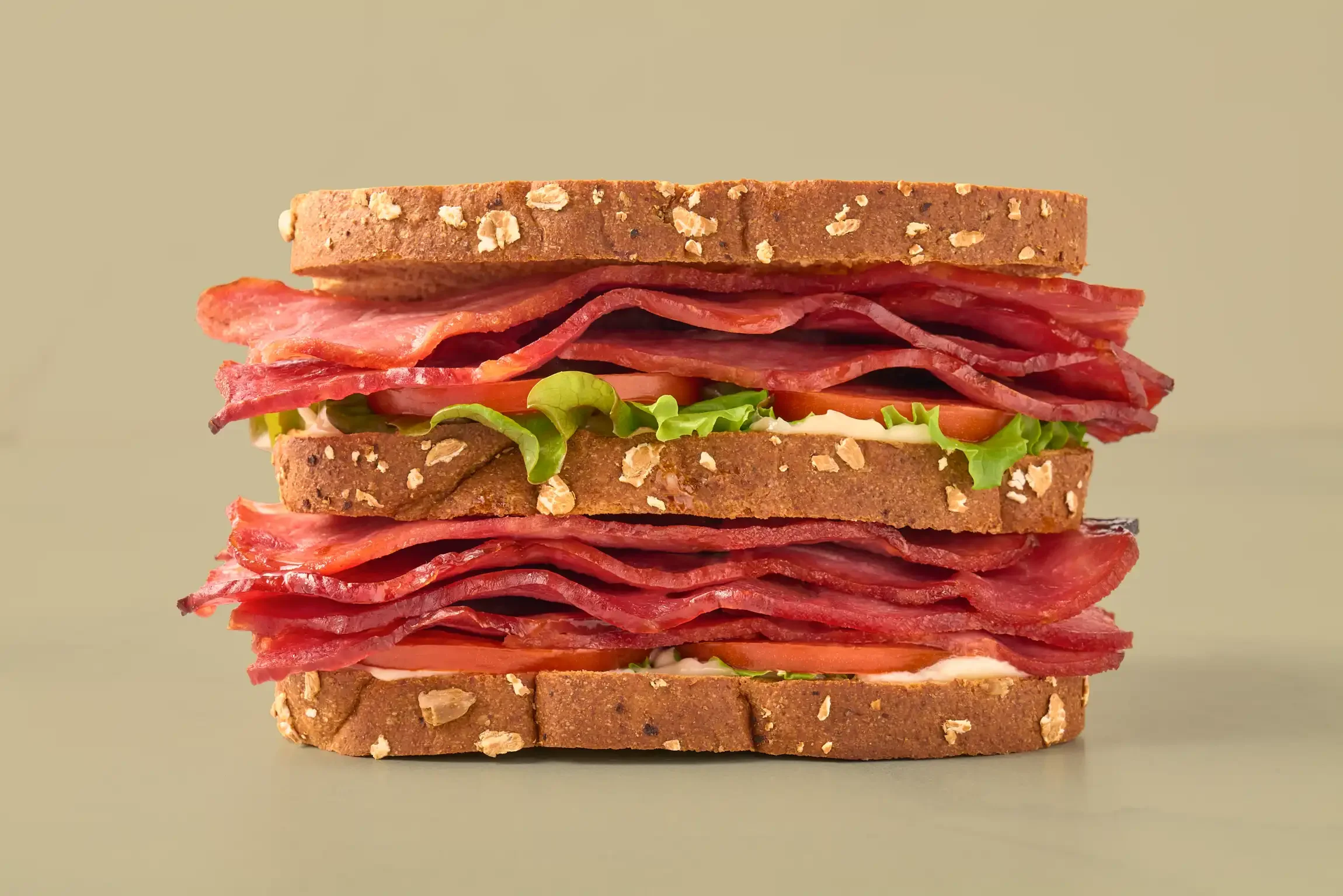 A close-up of a large BLT sandwich with multiple layers of bacon, lettuce, tomato, and whole grain bread slices. By Philadelphia, PA food photographer & food stylist team Bartholomew Studio.