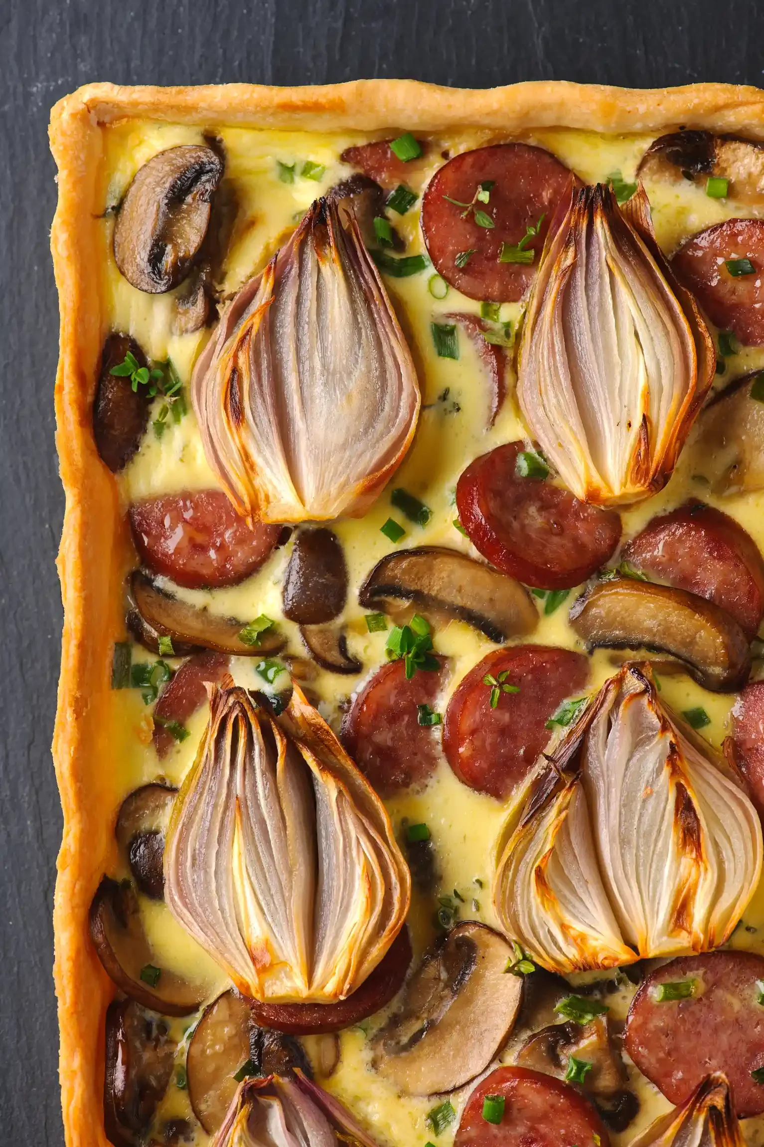 A vegetable quiche with a golden crust, filled with sliced mushrooms, roasted onions, cherry tomatoes, and herbs. By Philadelphia, PA & NJ food photographer & food stylist team Bartholomew Studio.