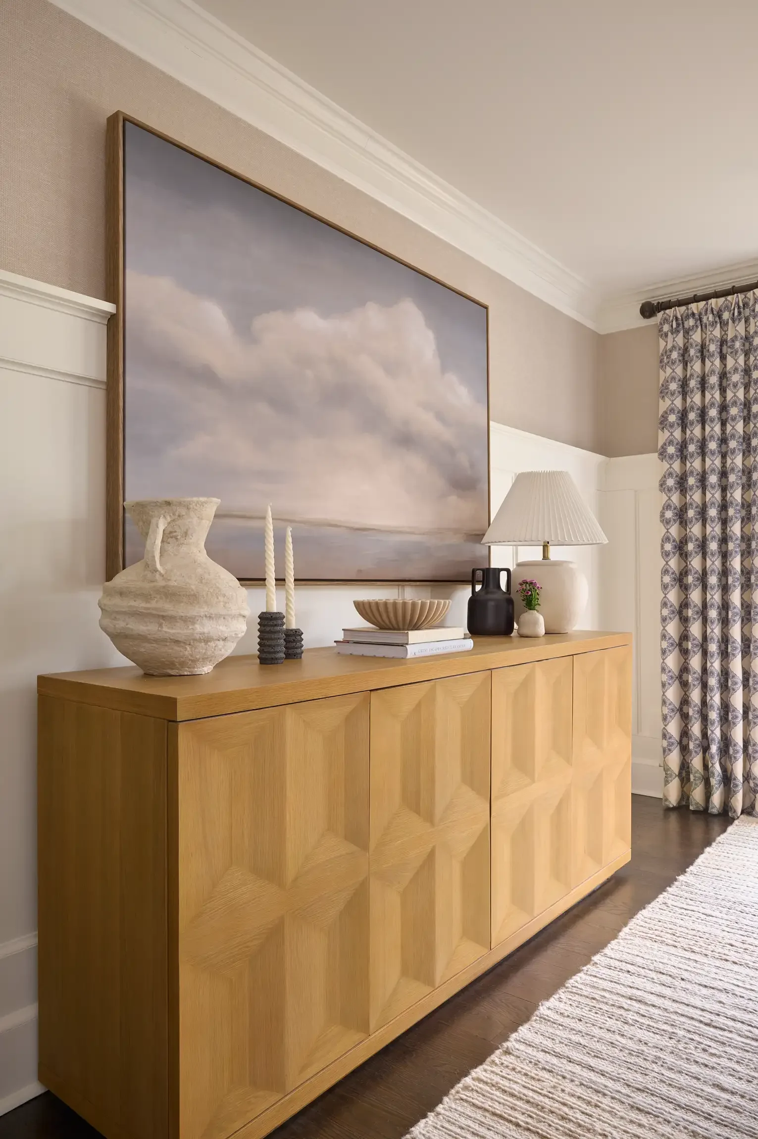 A wooden sideboard with decorative objects on top, a large framed sky photograph hanging above it, and a patterned curtain on the right. By interior design photographer Paul Bartholomew.