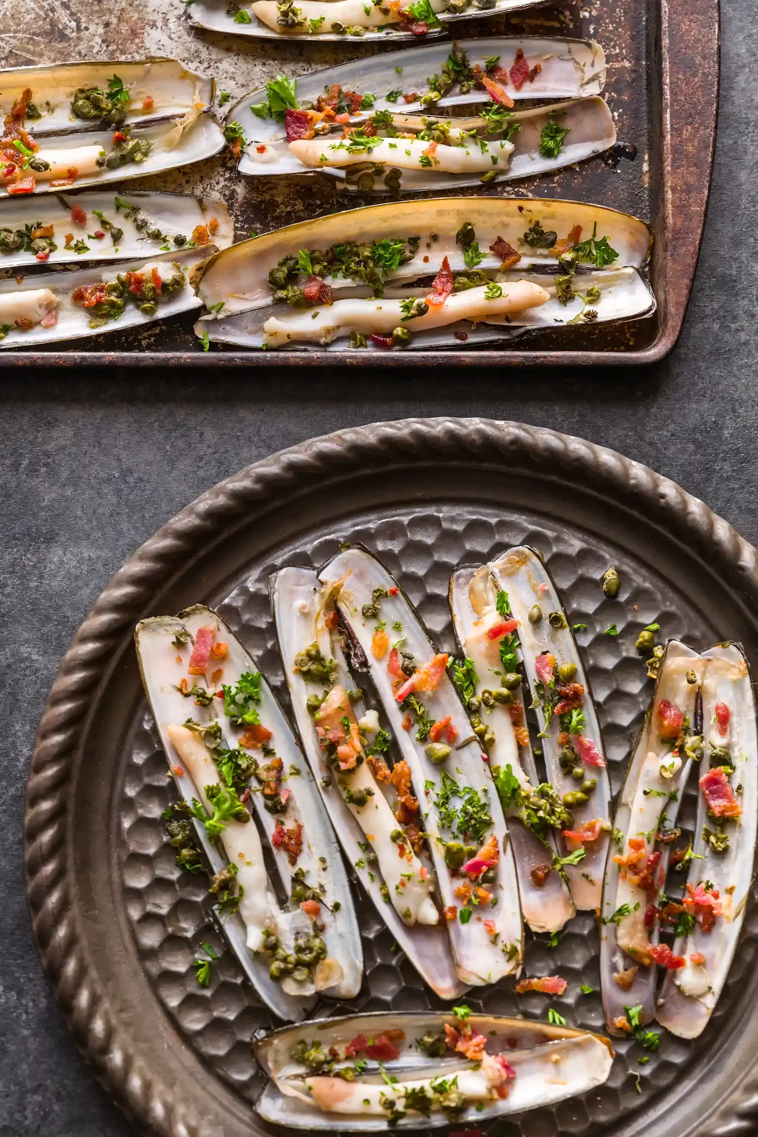 Razer clams topped with chopped herbs, served on a round metallic plate. By Pennsylvania & New Jersey food photographer & food stylist team Bartholomew Studio.
