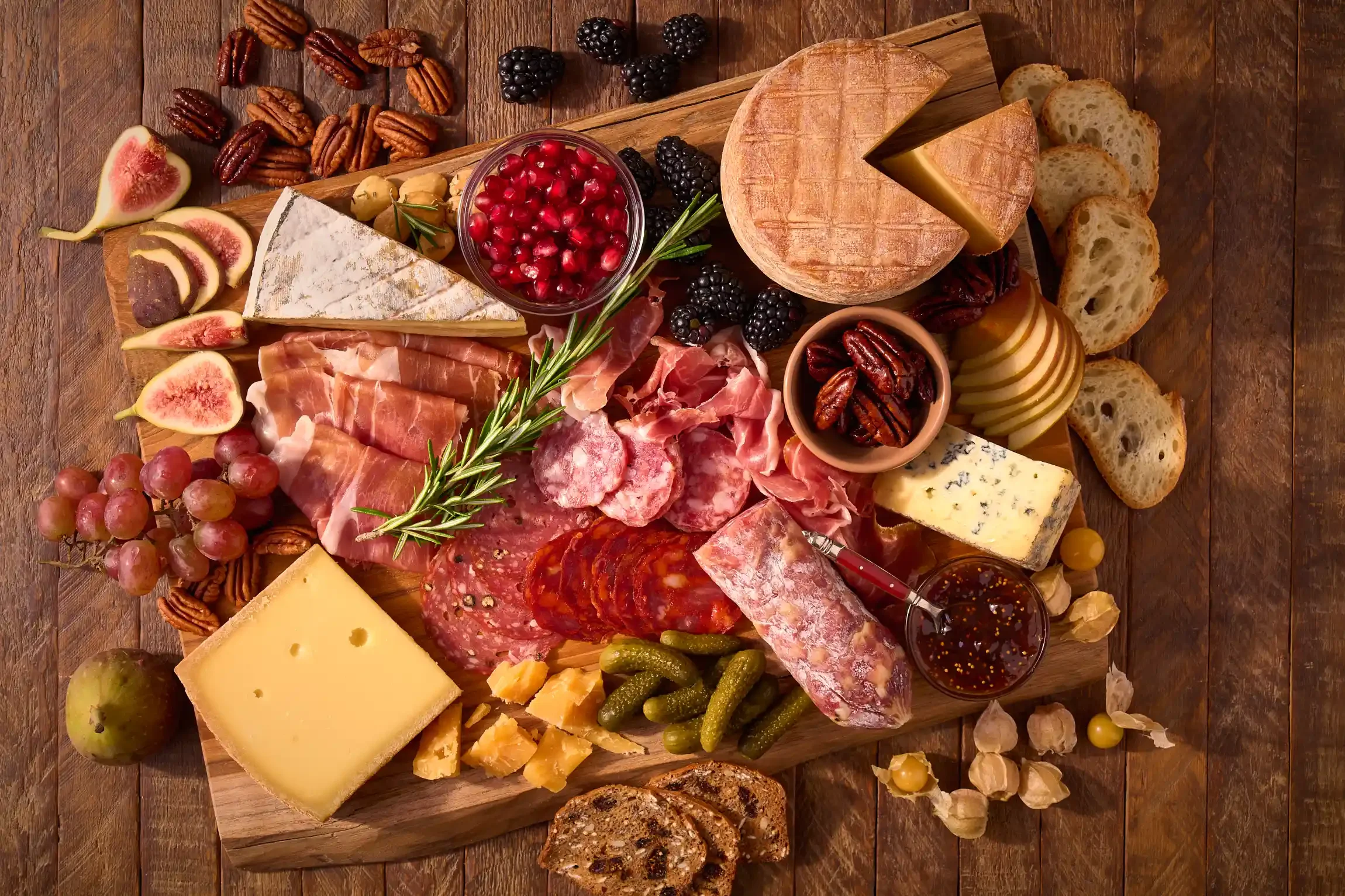 A classic meat and cheese charcuterie board with various cheeses, cured meats, fruits, nuts, and bread slices on a wooden surface. By PA, NJ & NY food photographer & food stylist team Bartholomew Studio.