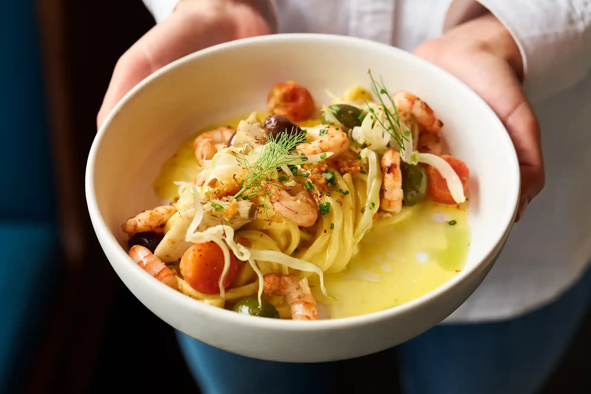 A bowl of pasta with shrimp, cherry tomatoes, olives, and garnished with herbs at a French restaurant. By NJ restaurant photographer Bartholomew Studio.