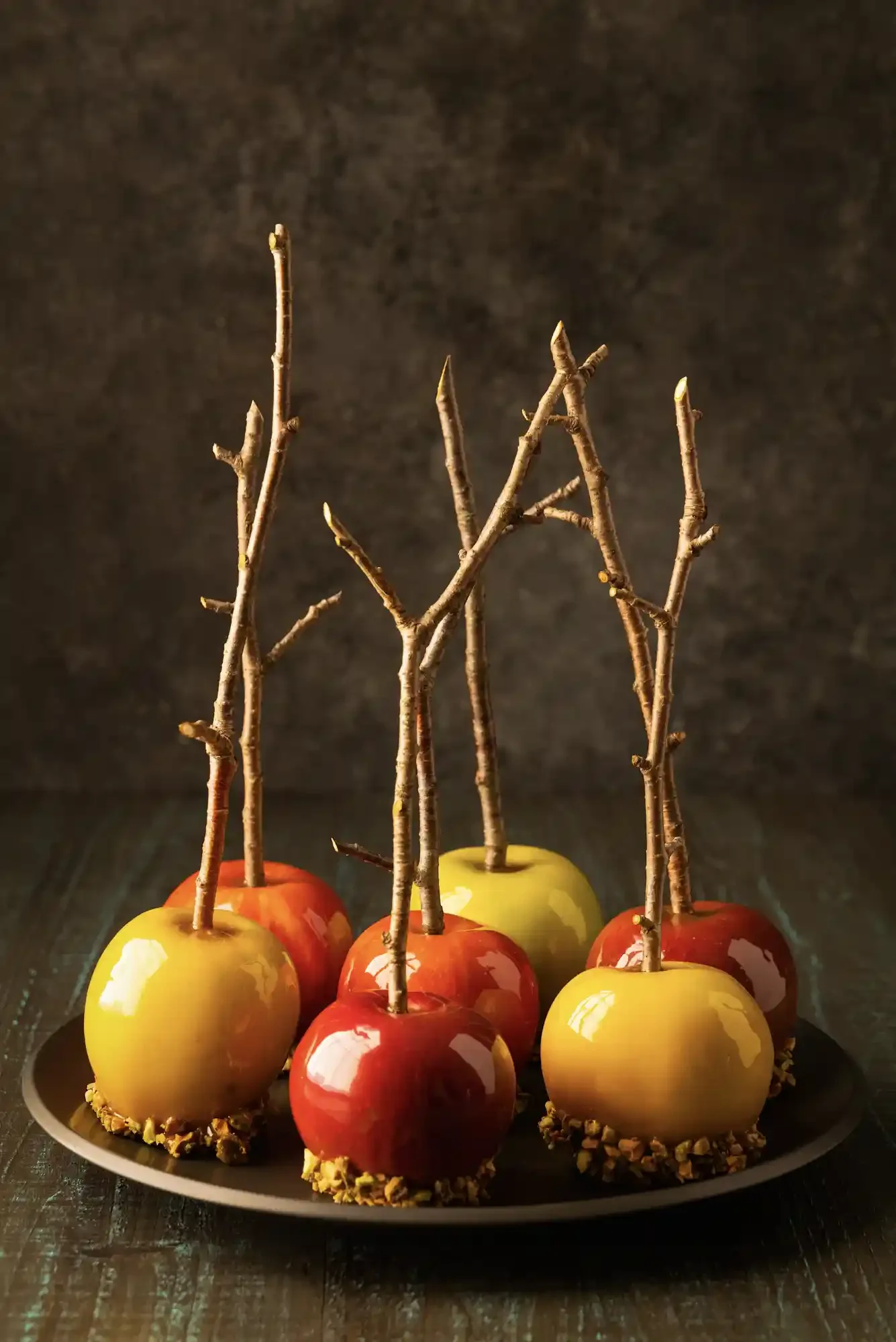 A plate of caramel candied apples with sticks, alternating red and yellow apples, garnished with chopped nuts at the bottom. Halloween them setting. By Philadelphia, PA, New Jersey food photographer & food stylist team Bartholomew Studio.