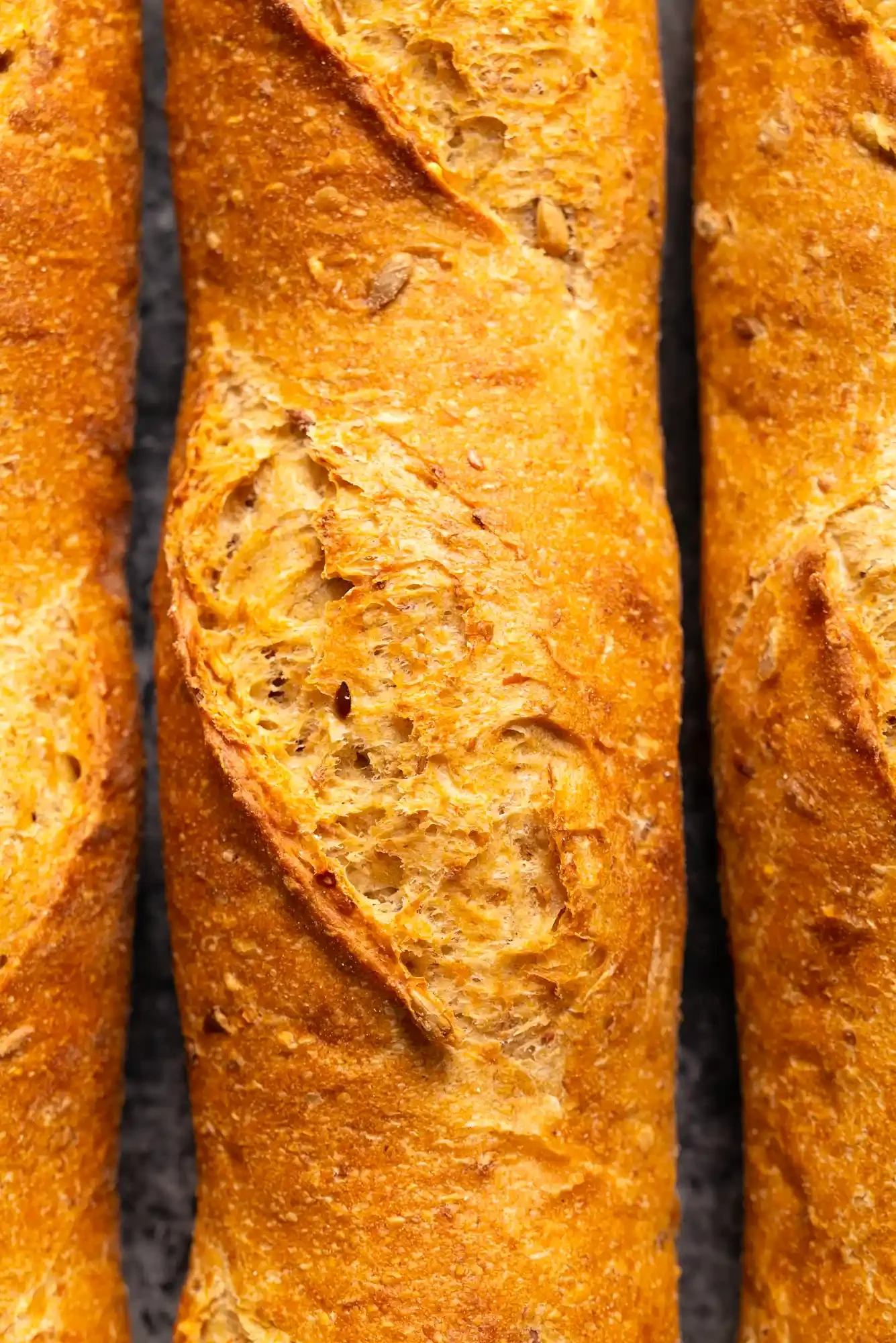 Close-up of three crispy baguette bread loaves with one in the center showing a rough, cracked surface and a crunchy texture. By Bucks County, PA food photographer & food stylist team Bartholomew Studio.