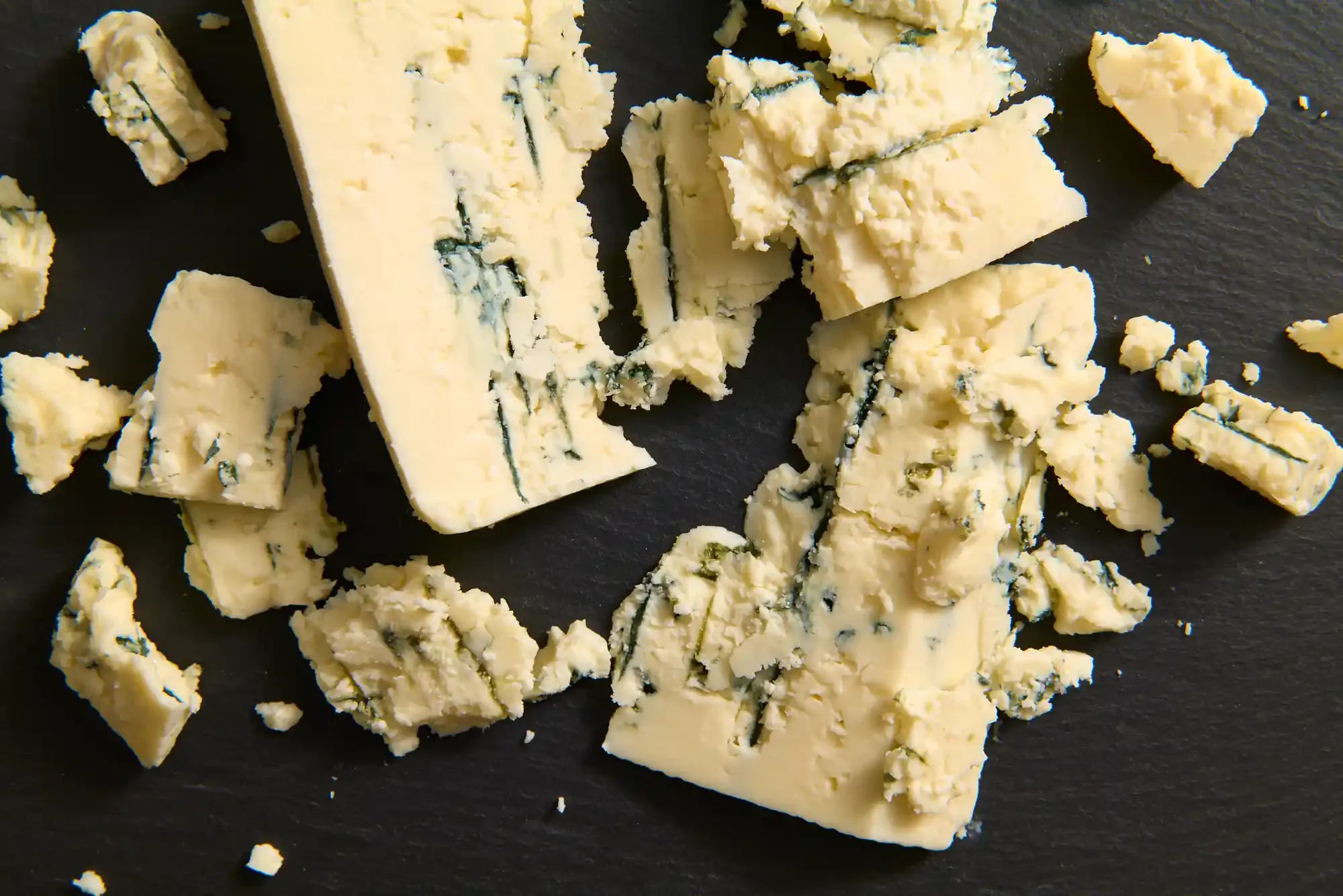 Crumbled blue cheese on a black surface. - By Philadelphia, PA food photographer & food stylist team Bartholomew Studio. By Philadelphia, PA food photographer & food stylist team Bartholomew Studio.