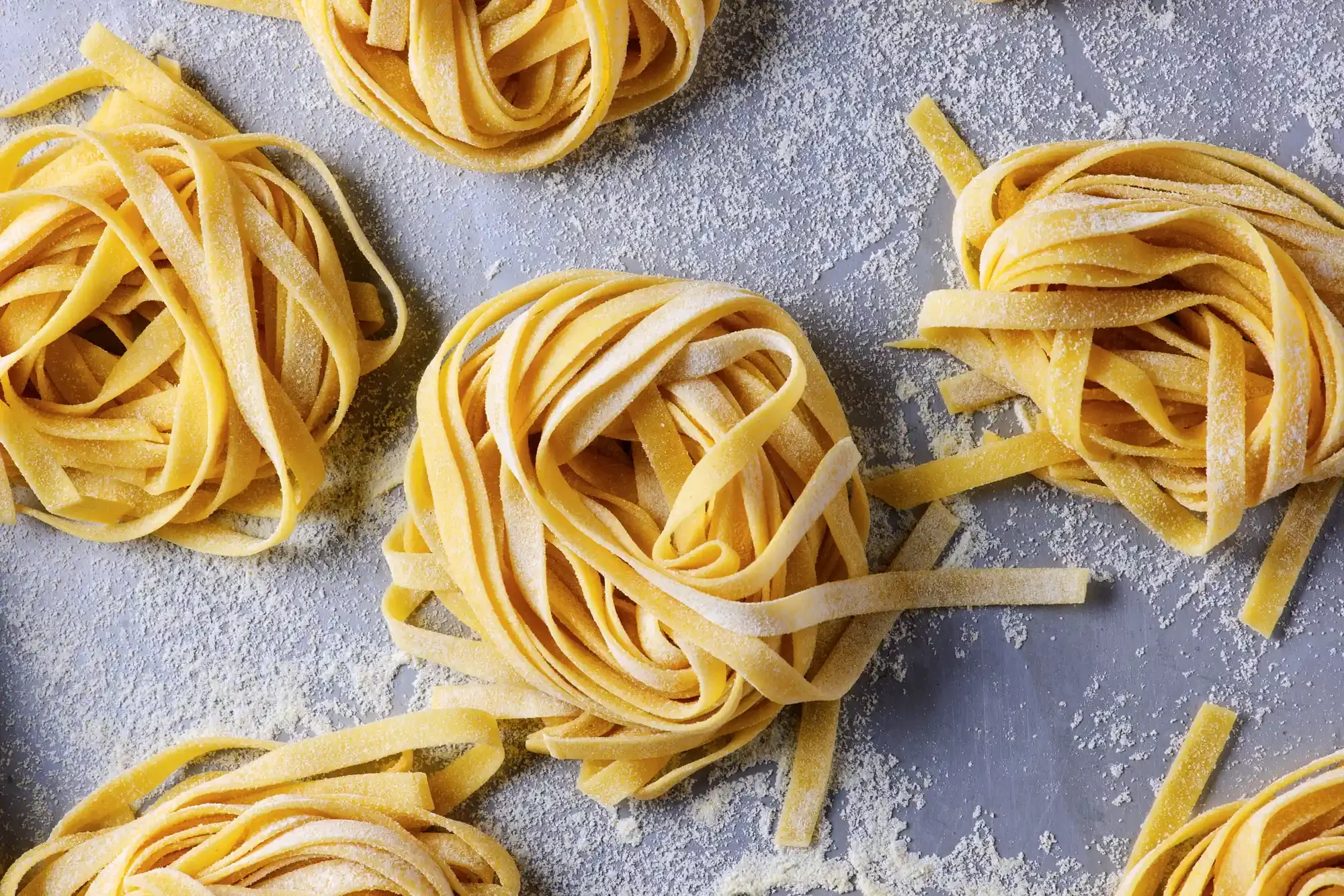 Multiple nests of uncooked fettuccine pasta coated lightly with flour on a gray surface. By Philadelphia, PA food photographer & food stylist team Bartholomew Studio.