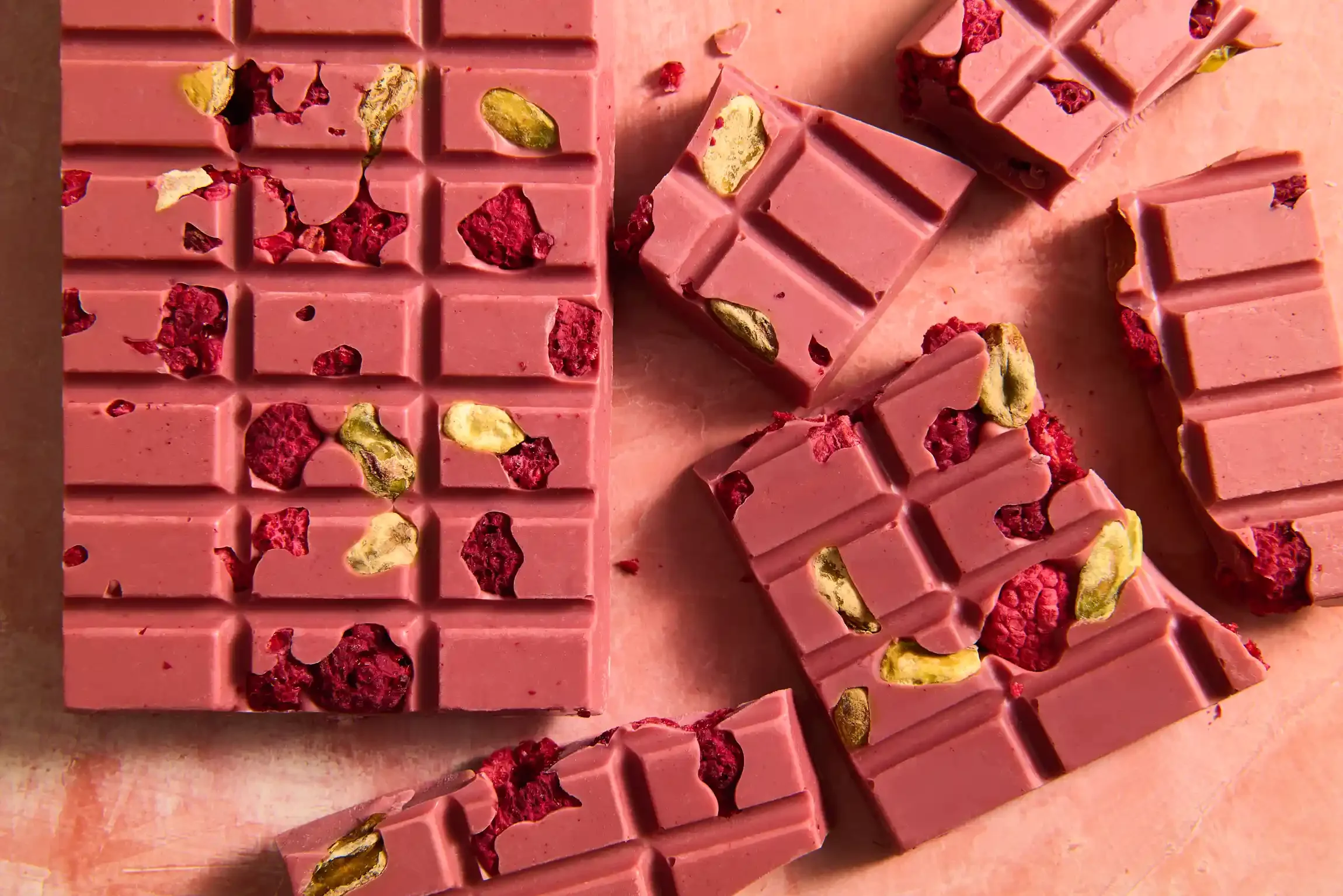 Pieces of pink chocolate with dried raspberry and pistachio nuts on a pink background. By Philadelphia, PA & NJ chocolate photographer & food stylist team Bartholomew Studio.