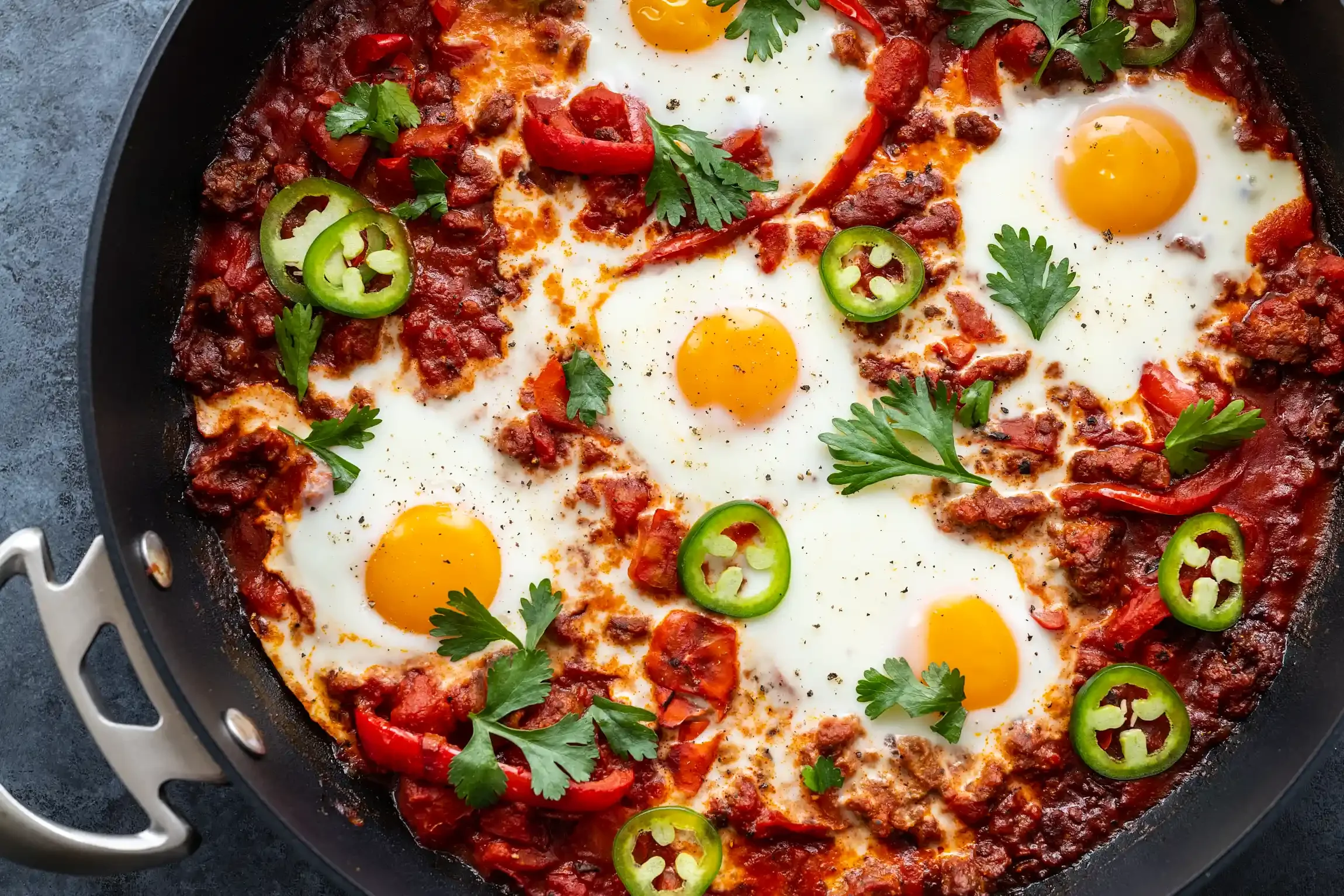 Spanish eggs topped with chopped red and green chili peppers, cilantro, and sausage in a tomato sauce. By Philadelphia, PA & NJ food photographer & food stylist team Bartholomew Studio.