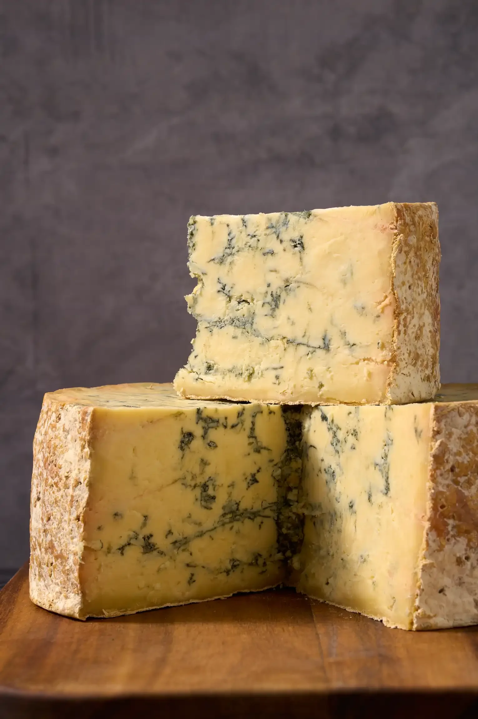 Blue cheese stacked on a wooden surface, with a dark background. By Pennsylvania Food Photographer & Stylist Team.