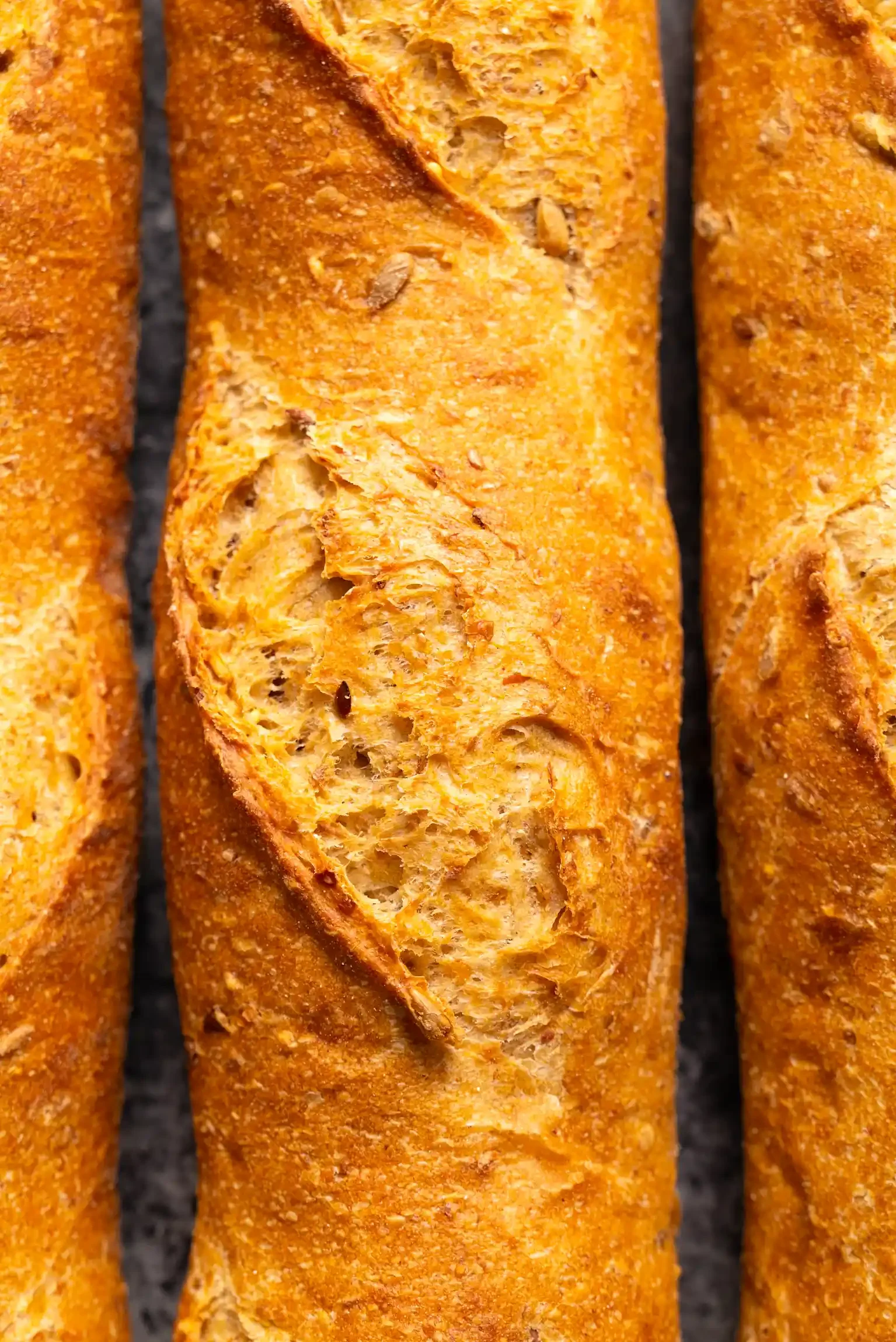 Close-up of three toasted bread baguettes on a dark surface, with one baguette sliced open to show the crust and texture inside. By Philadelphia, PA food photographer & food stylist team Bartholomew Studio.
