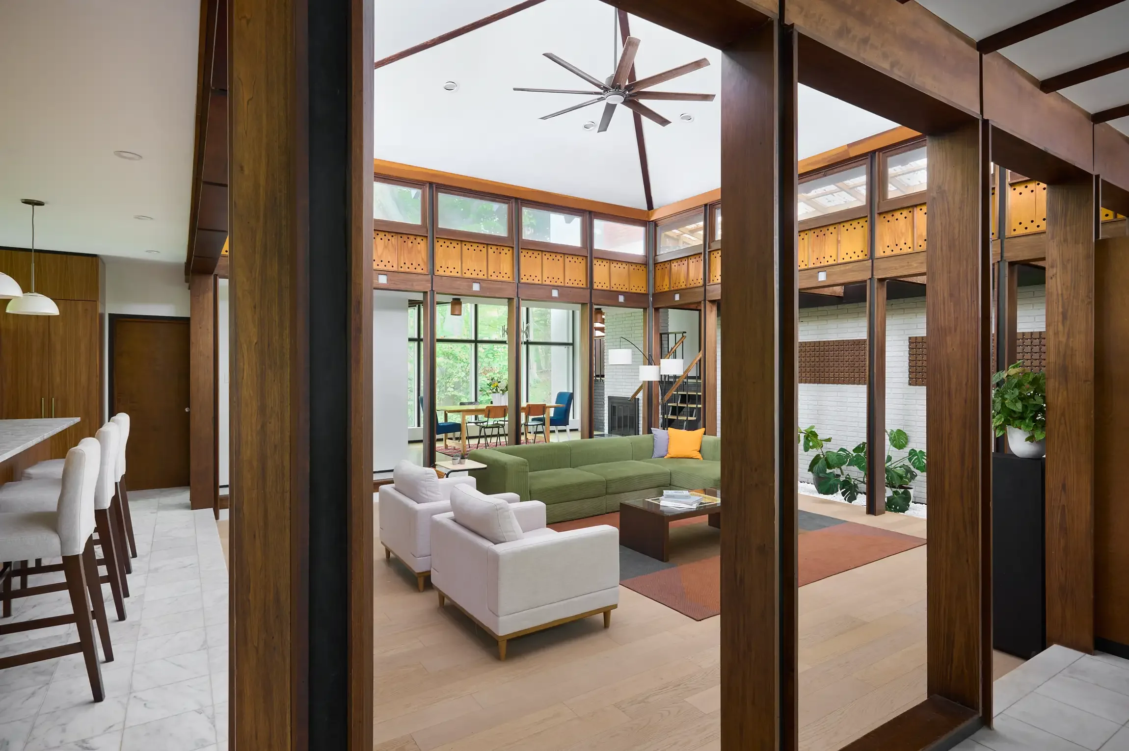 Spacious living room with wood beams, large windows, and modern furniture including a green sofa, white armchairs, and a wooden coffee table. By interior design photographer Paul Bartholomew.